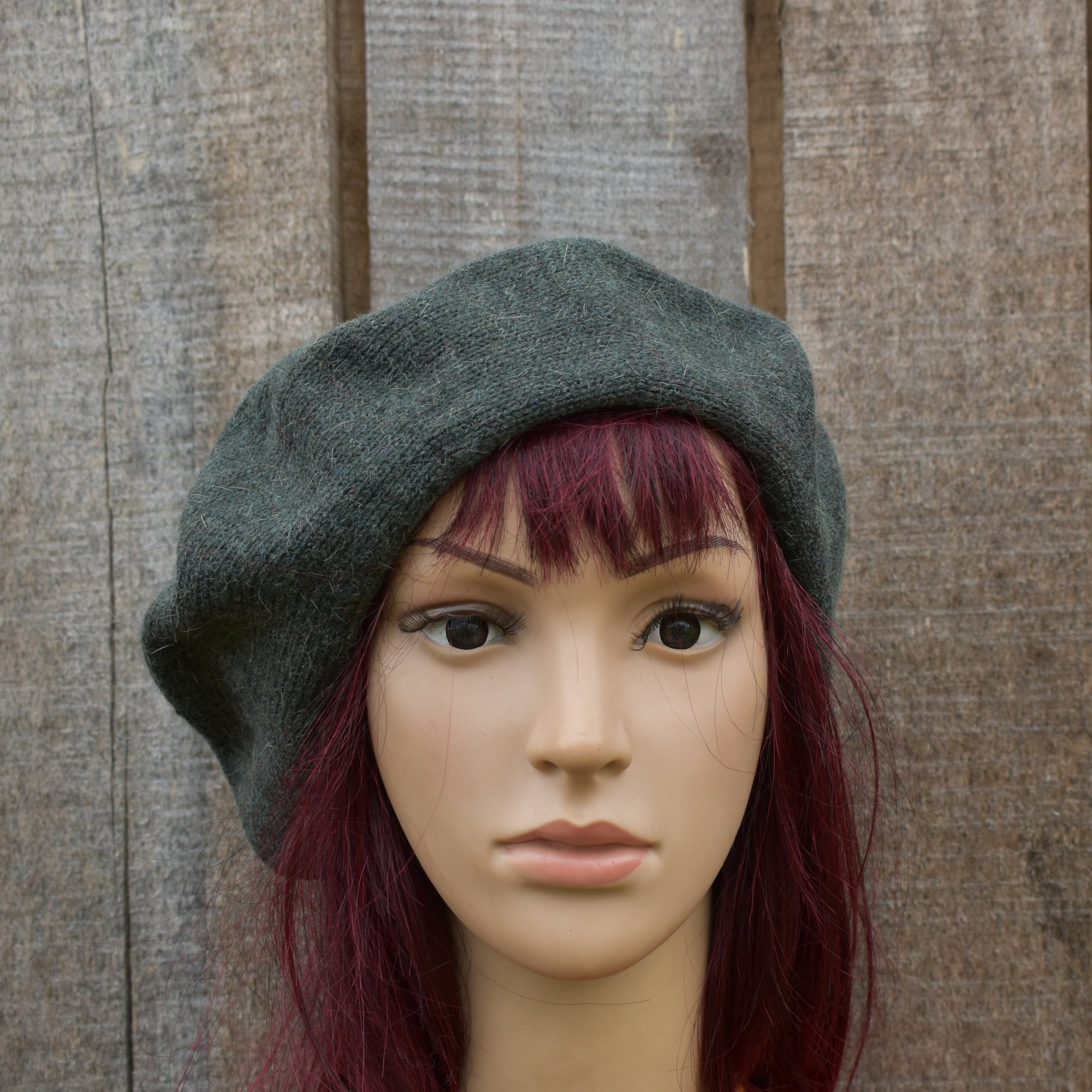 Mannequin head wearing a gray beret against a wooden background