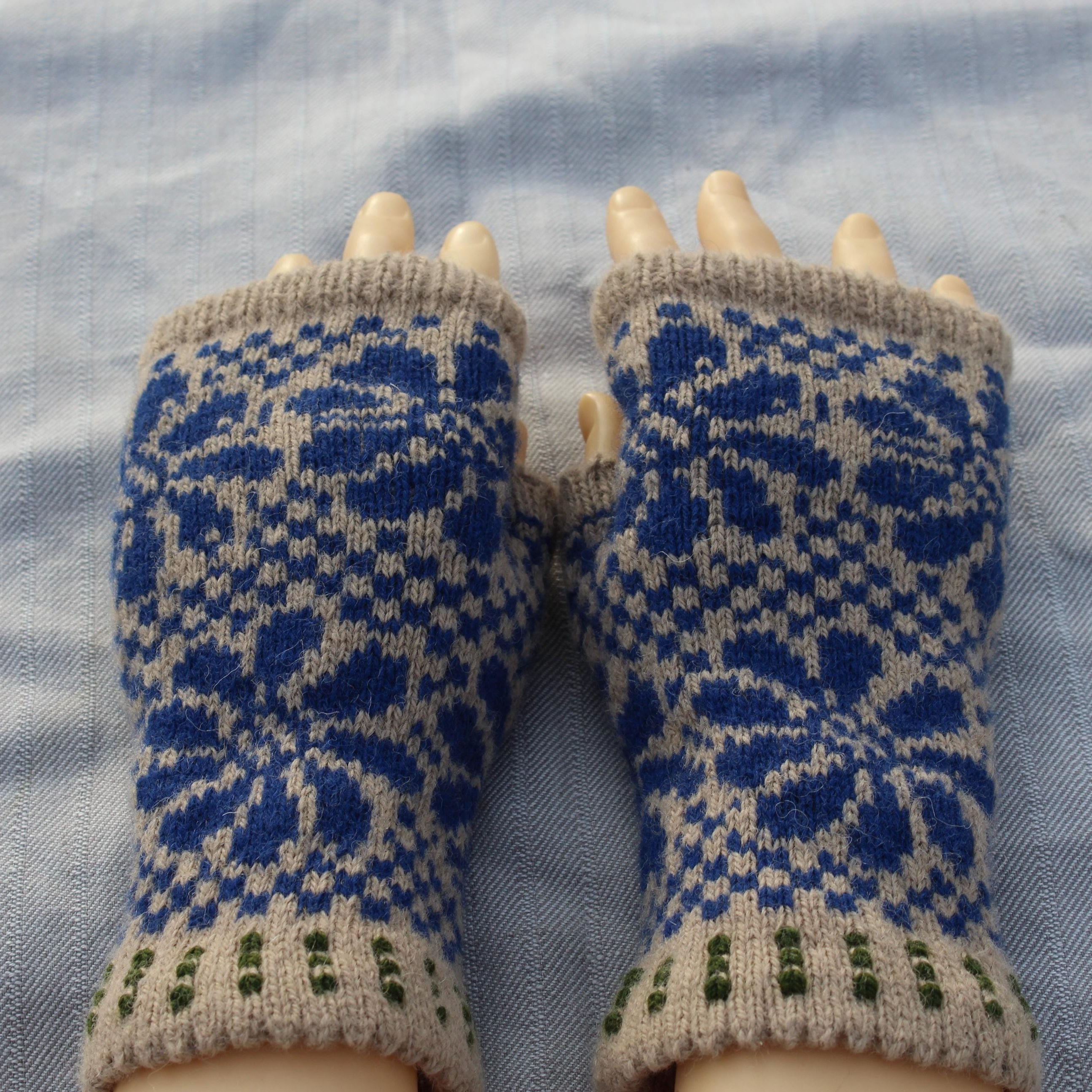 Pair of blue and beige patterned fingerless gloves on a blue fabric background