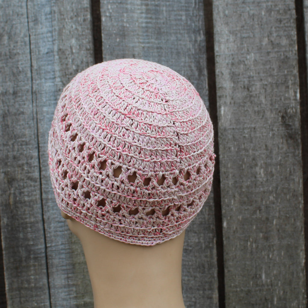 Pink crochet hat on a mannequin head against a wooden background