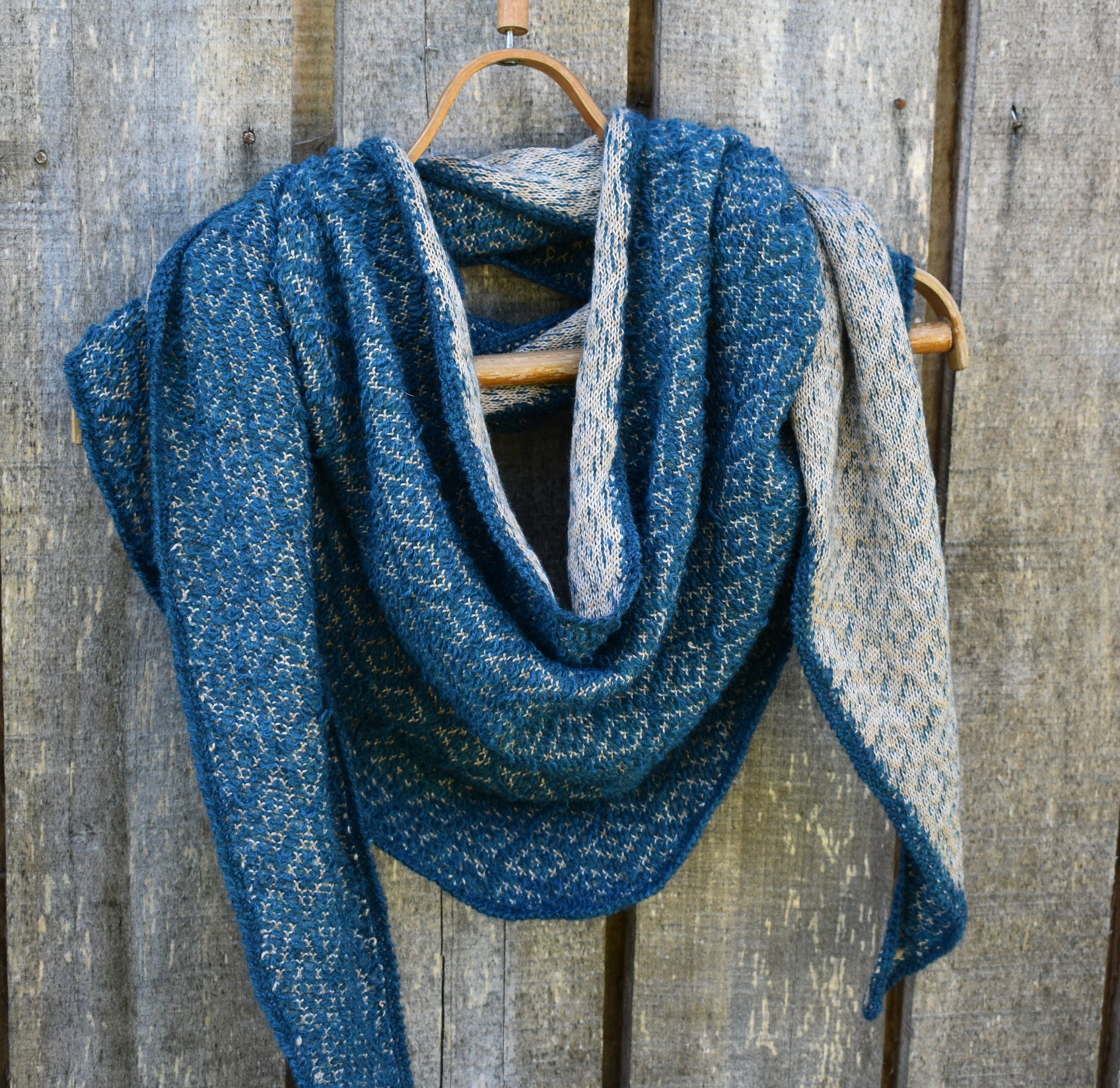 Blue and gray knitted scarf on a wooden hanger against a wooden background