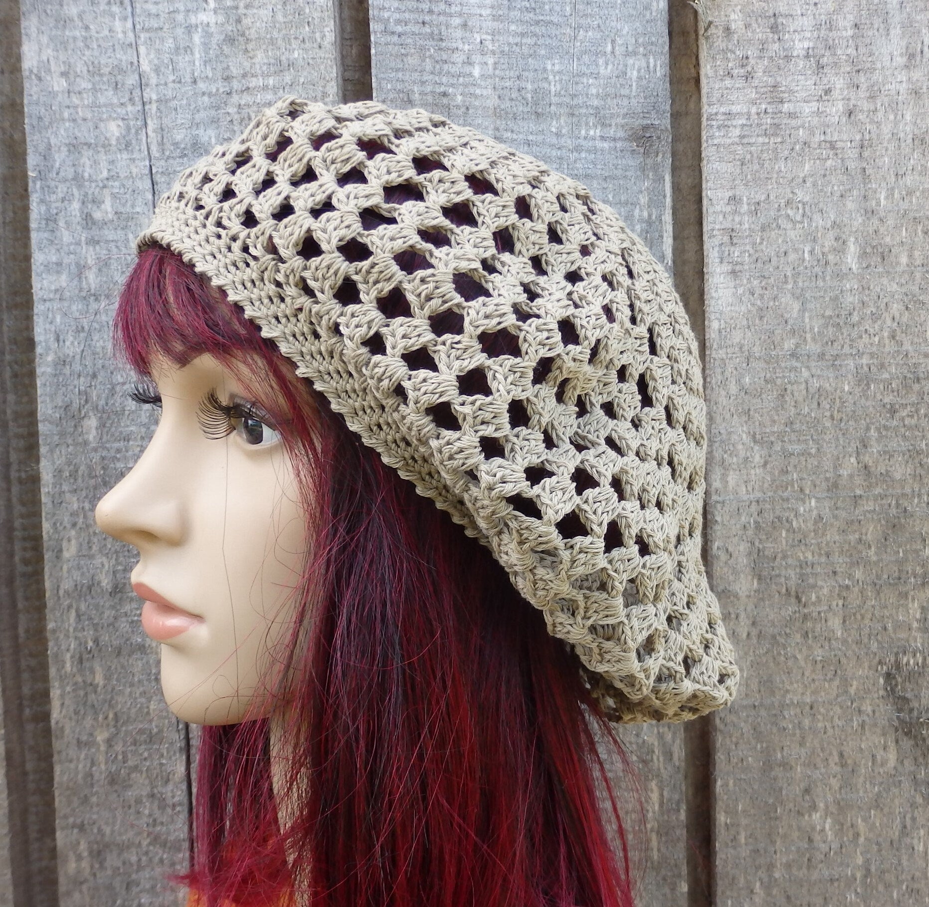 Mannequin head wearing a beige crochet hat against a wooden background