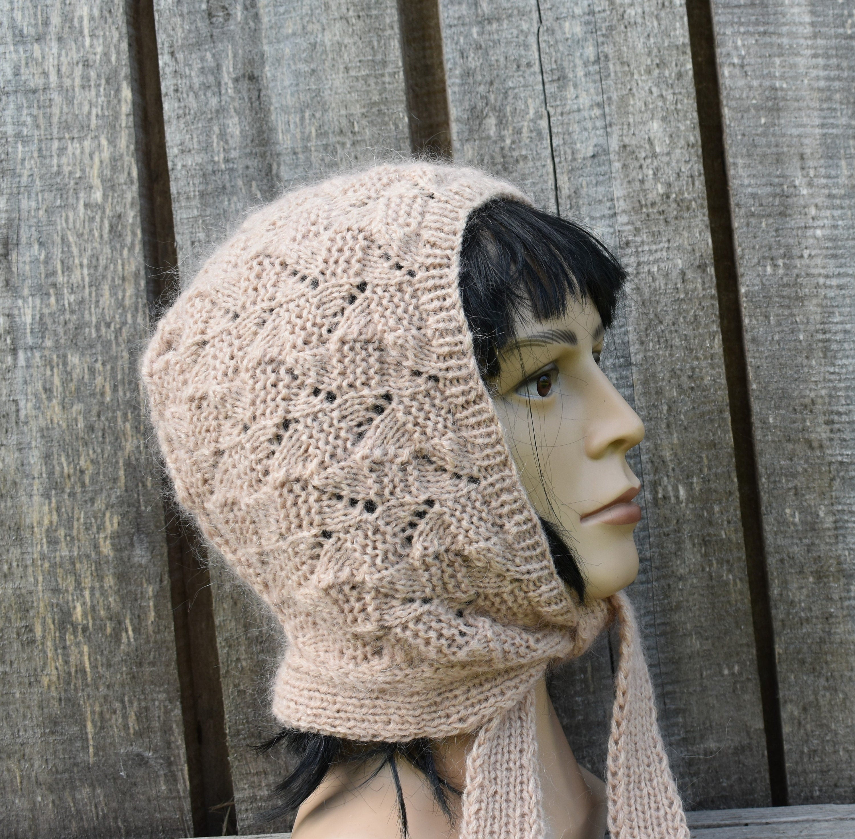Mannequin head wearing a beige knitted hood against a wooden background