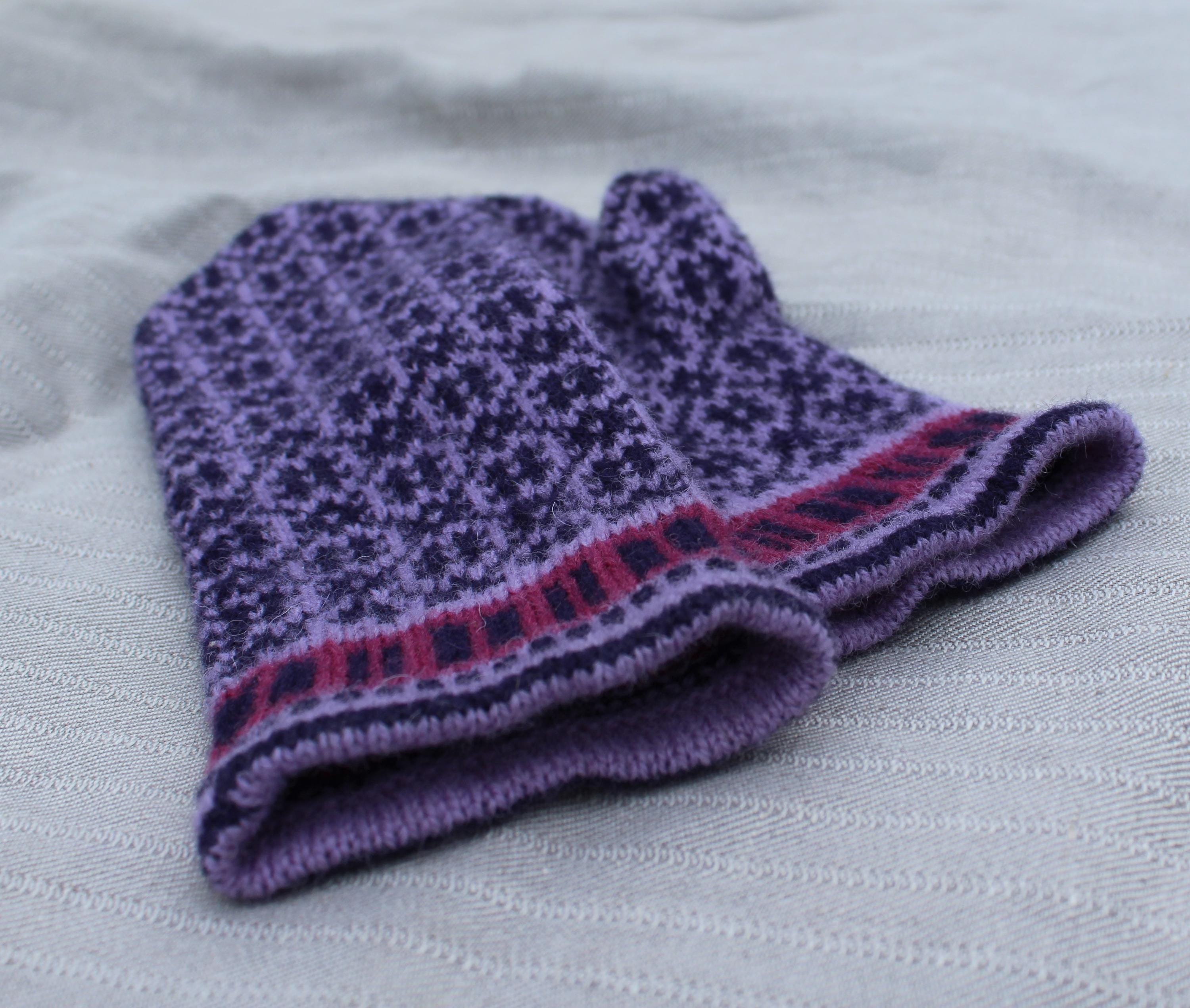 Knitted purple mitten with a pattern on a white fabric background