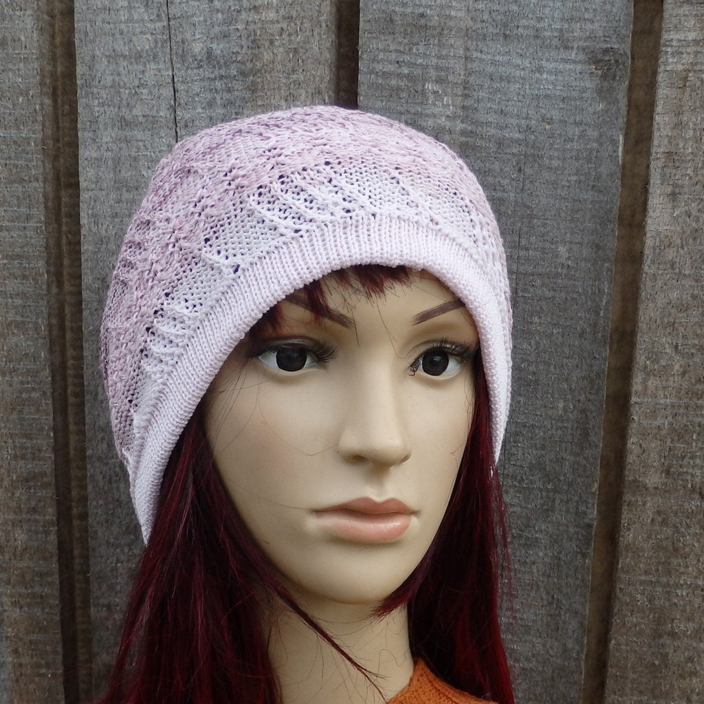 Mannequin head wearing a light purple knitted hat against a wooden background