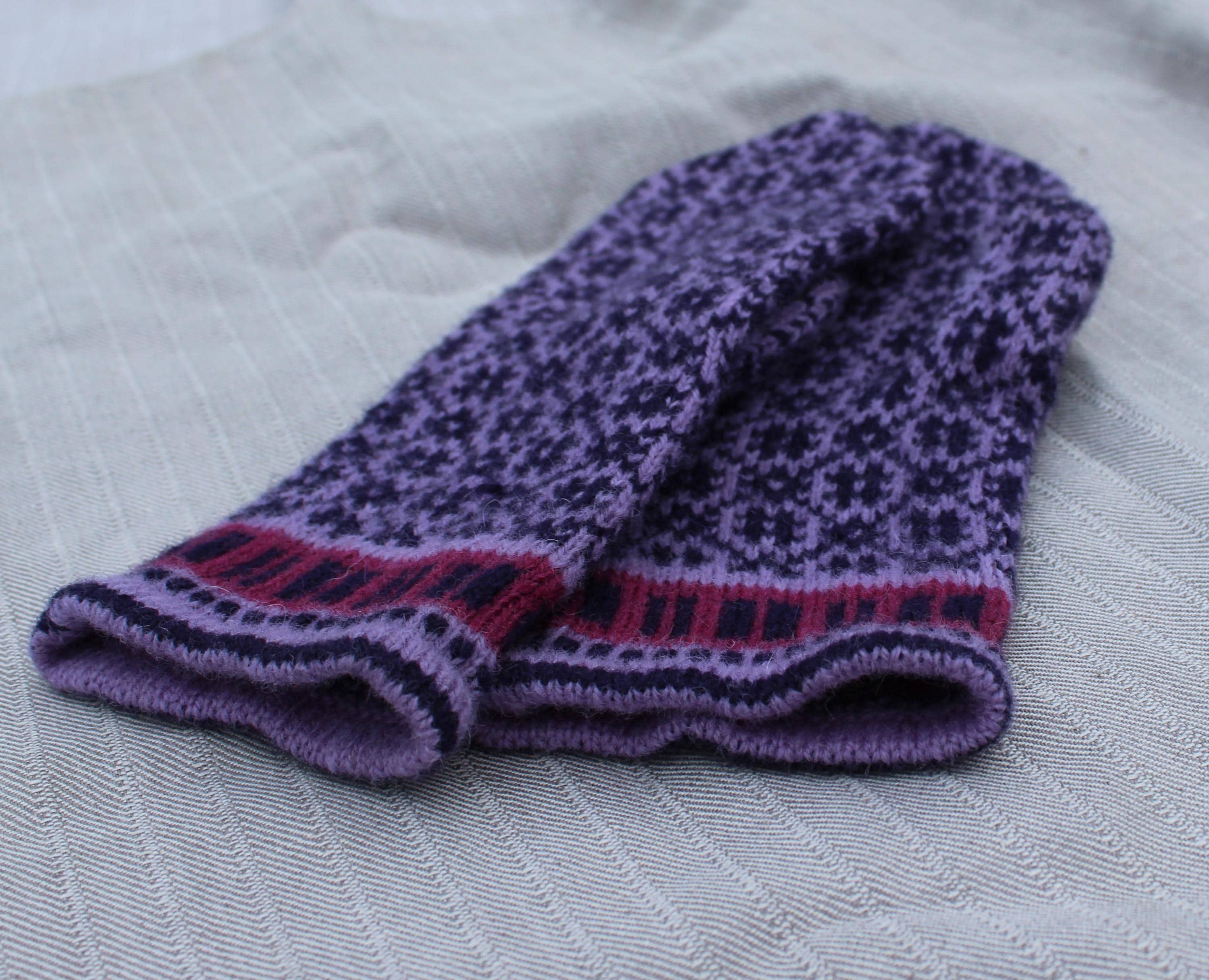 Knitted purple and pink patterned sock on a textured surface