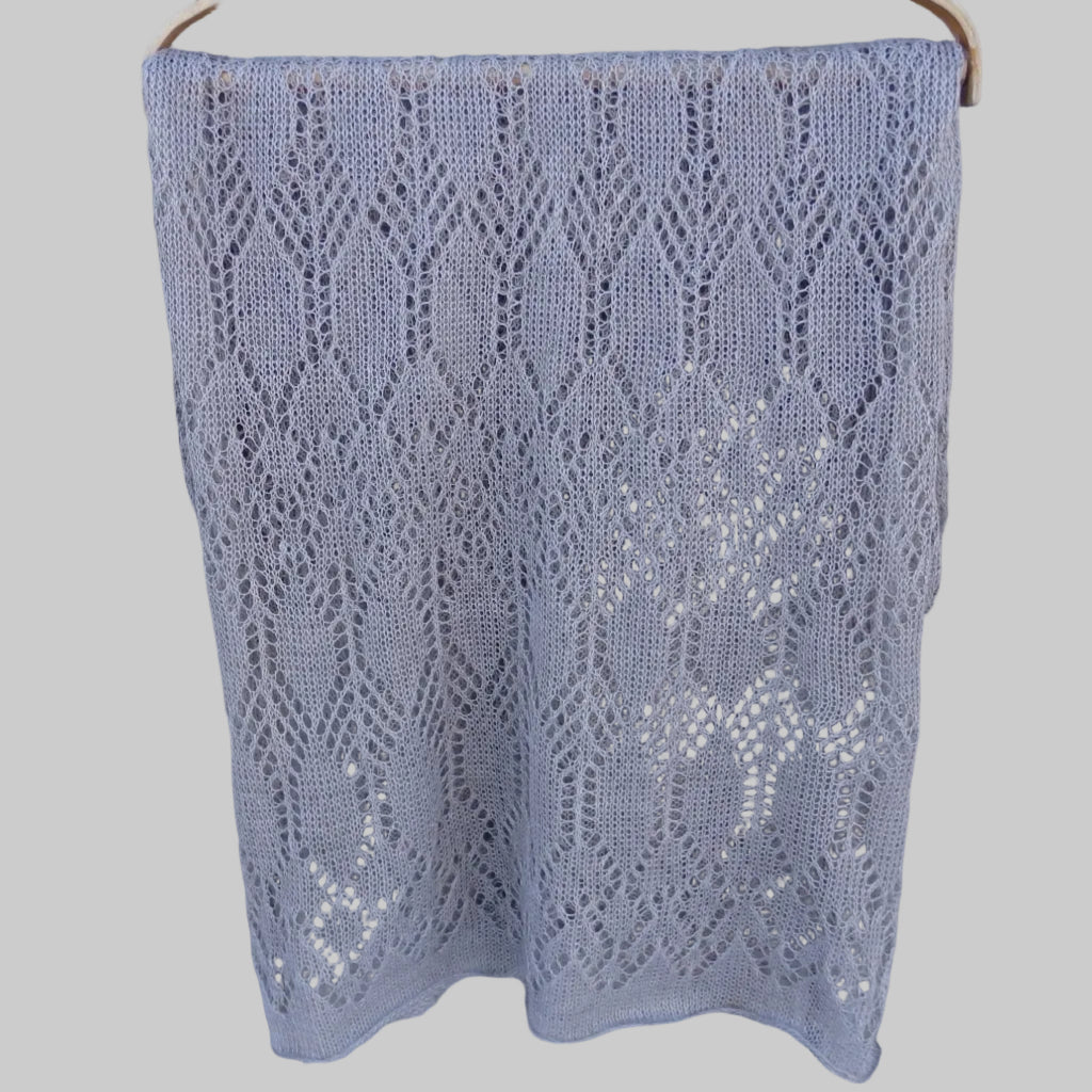 Knitted lace shawl on a wooden hanger against a wooden background
