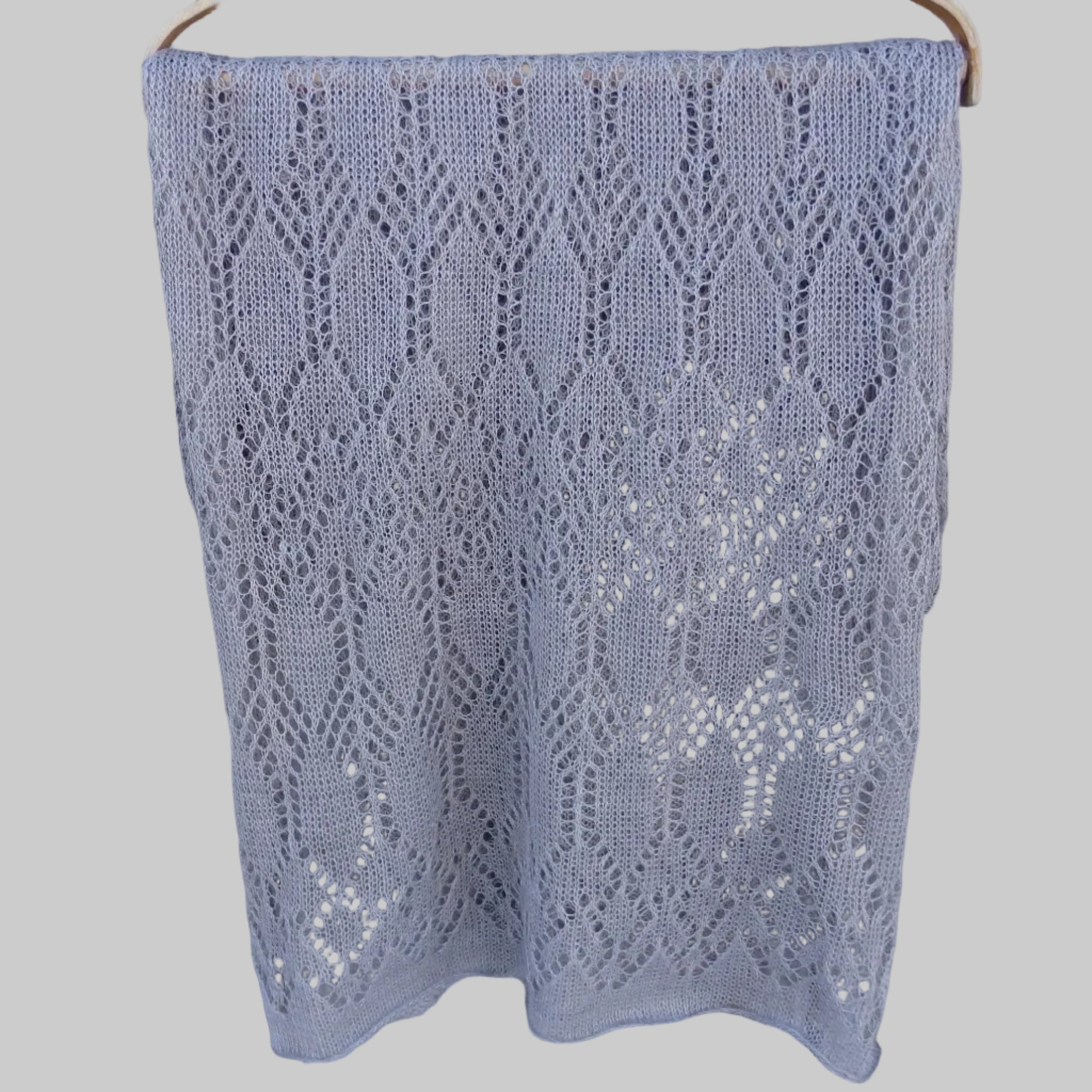 Knitted lace shawl on a wooden hanger against a wooden background