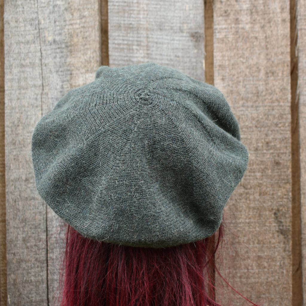 Grey knit beret on a person with red hair against a wooden background