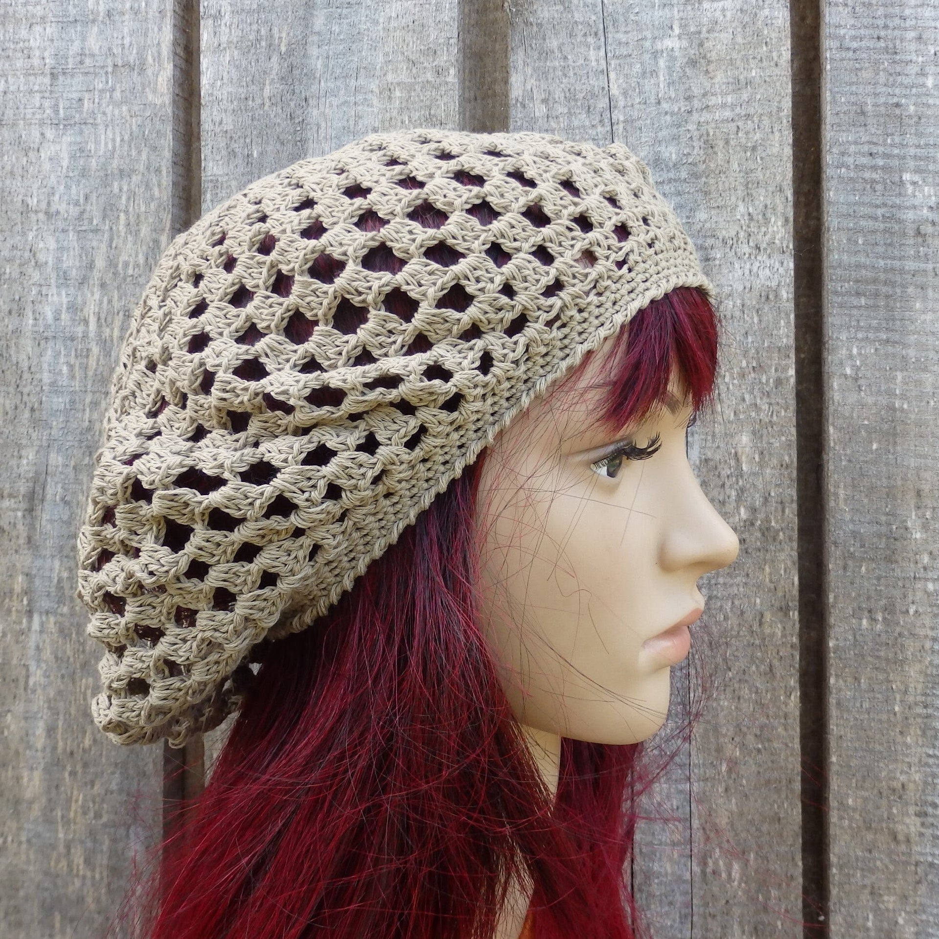 Beige crochet hat worn by a person with red hair against a wooden background