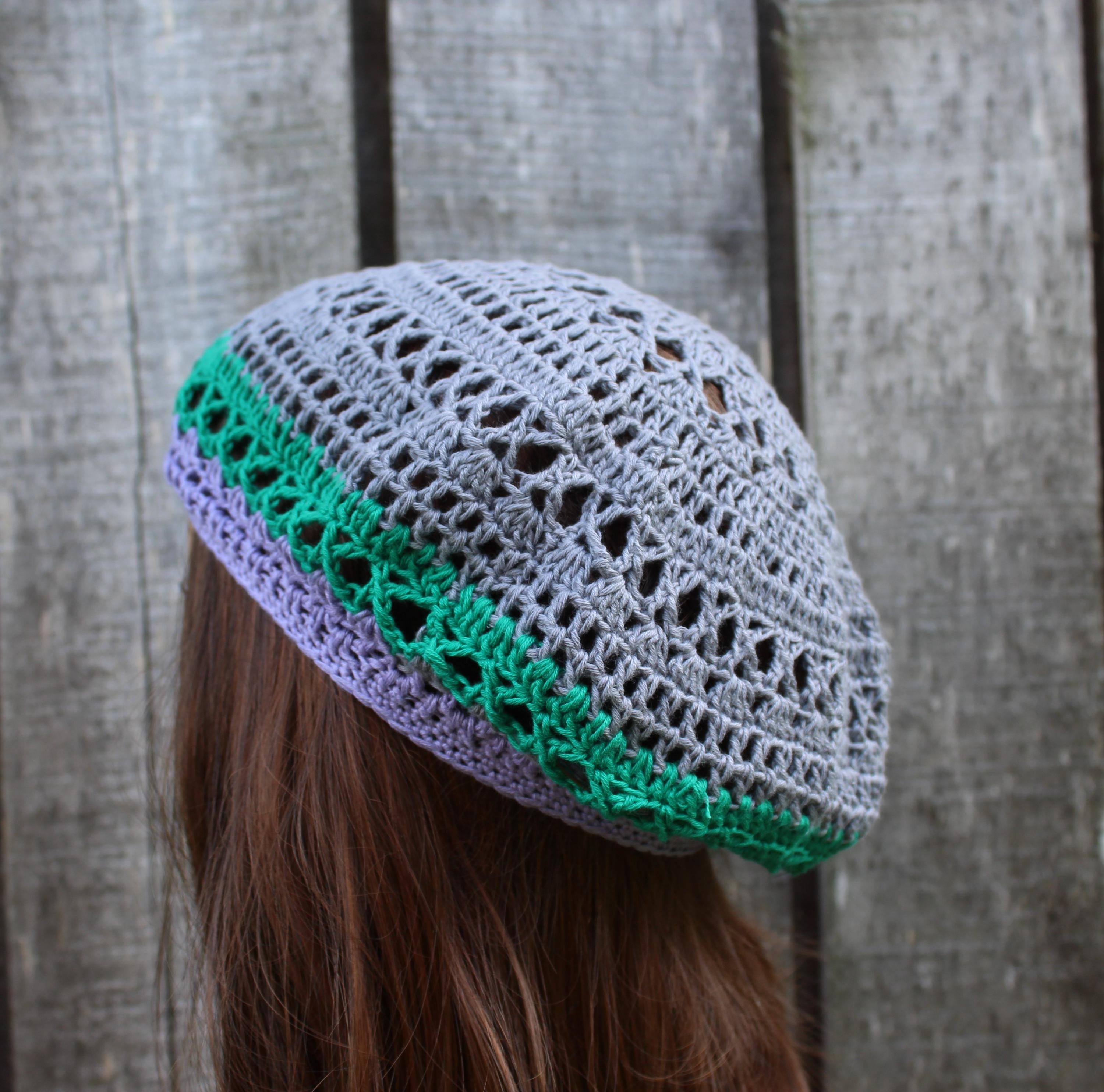 Gray and green crocheted beret worn by a person against a wooden fence background
