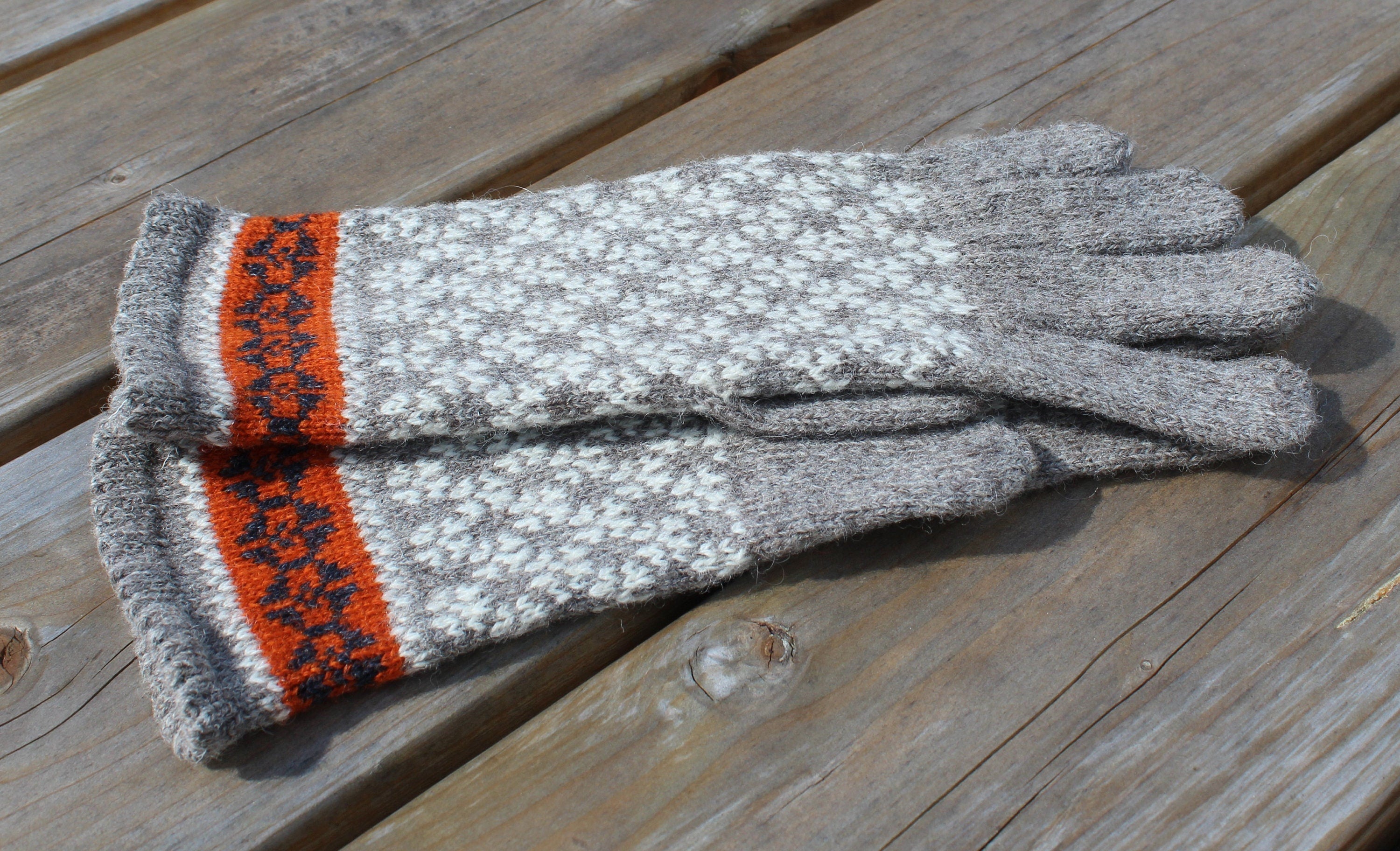 Pair of gray gloves with orange and white pattern on a wooden surface