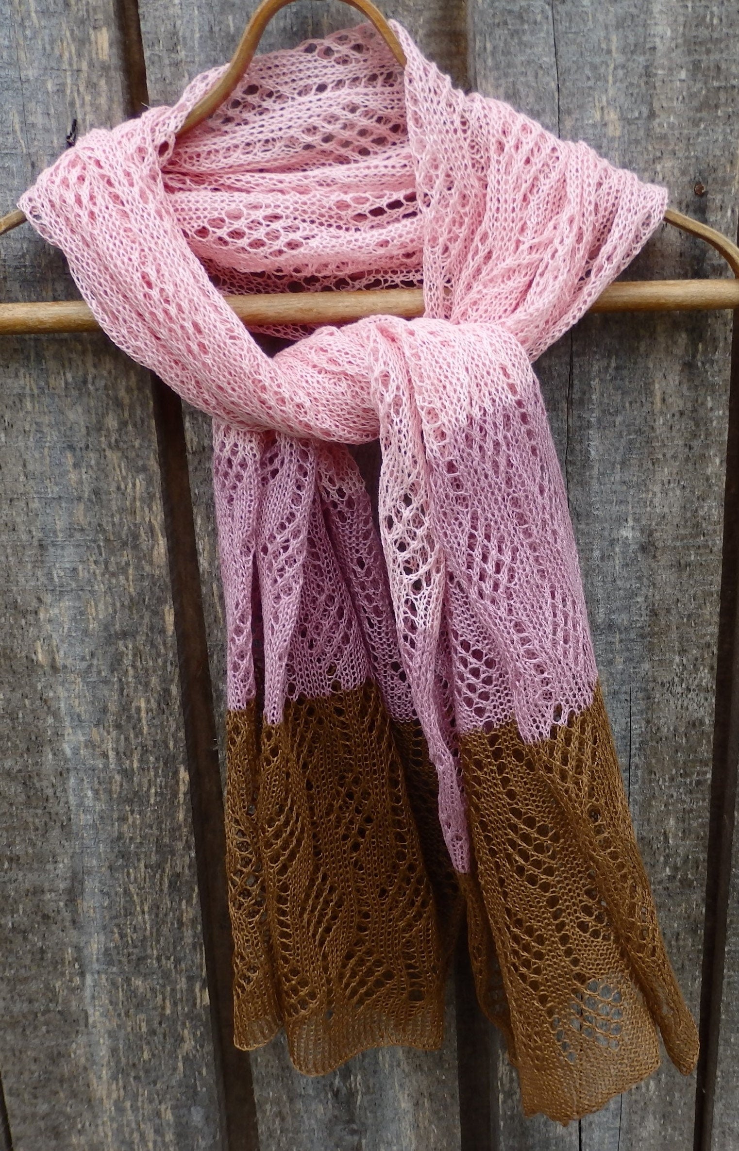 Pink and brown knitted scarf on a wooden hanger against a rustic wooden background