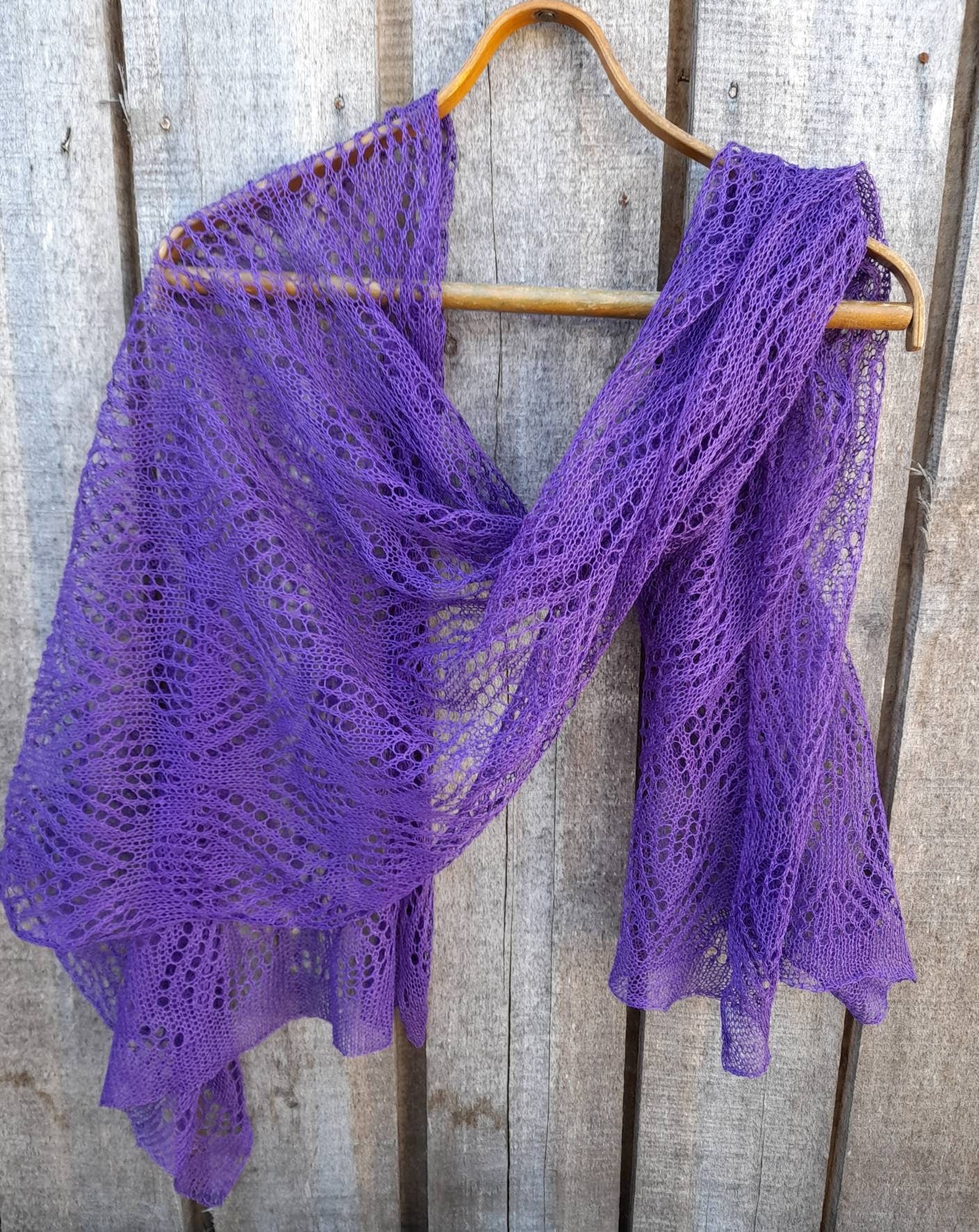 Purple knitted shawl on a wooden hanger against a wooden background