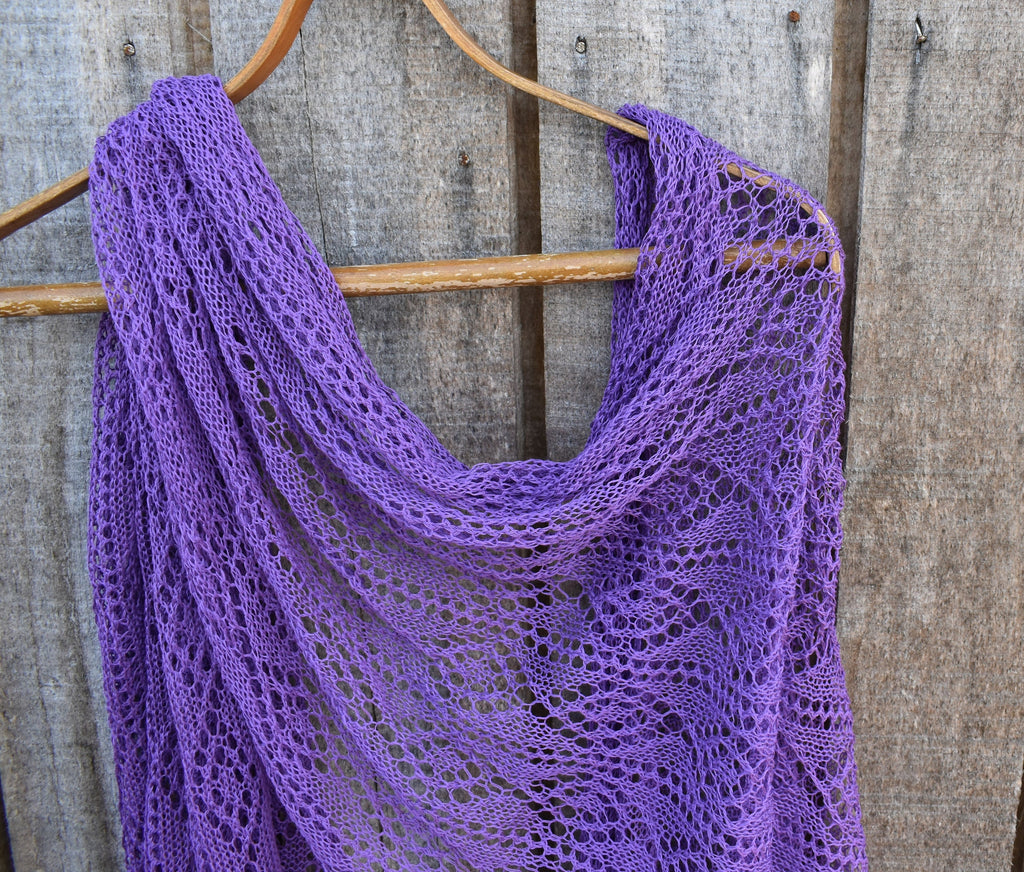 Purple knitted shawl on a wooden hanger against a rustic wooden background