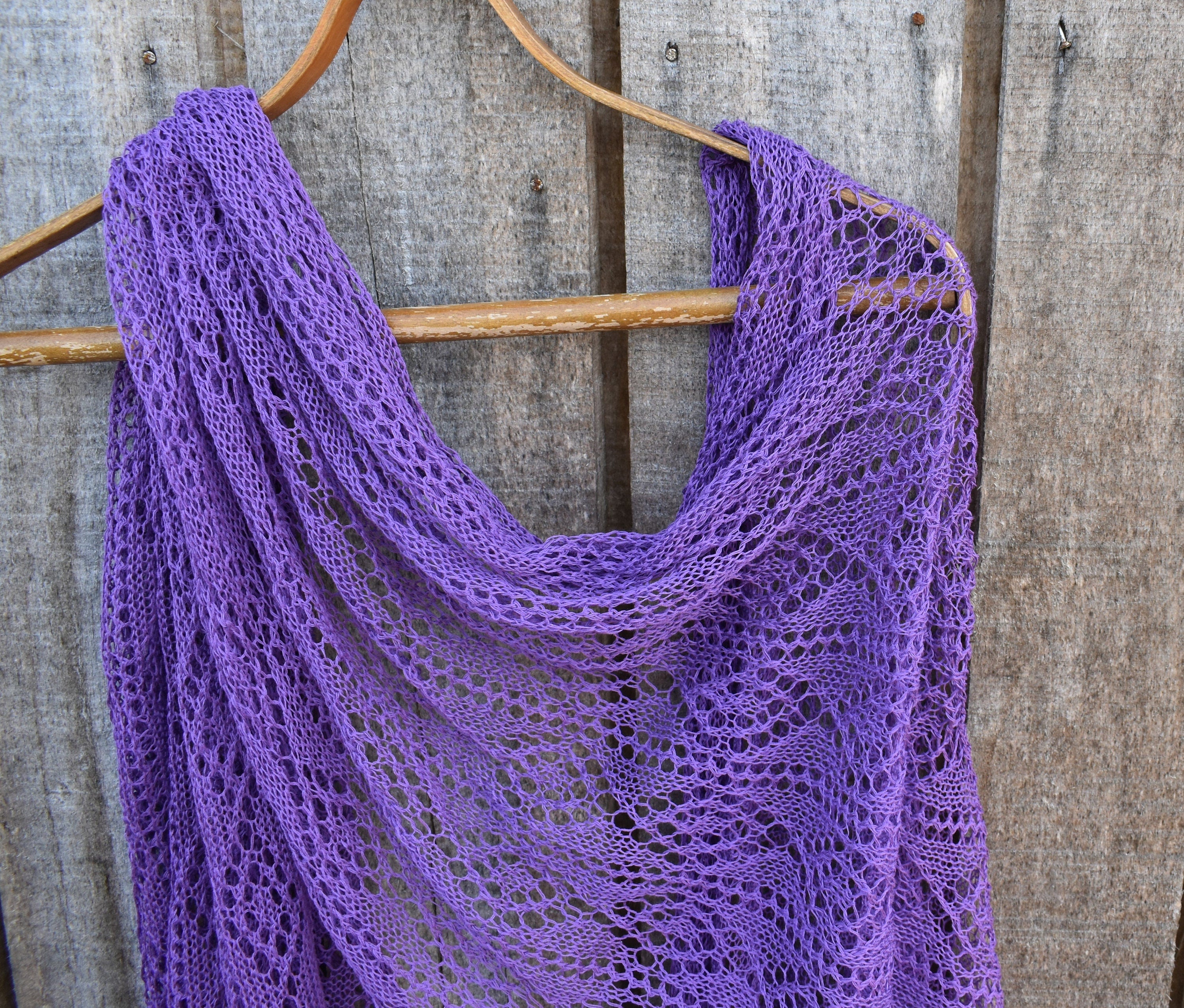 Purple knitted shawl on a wooden hanger against a rustic wooden background