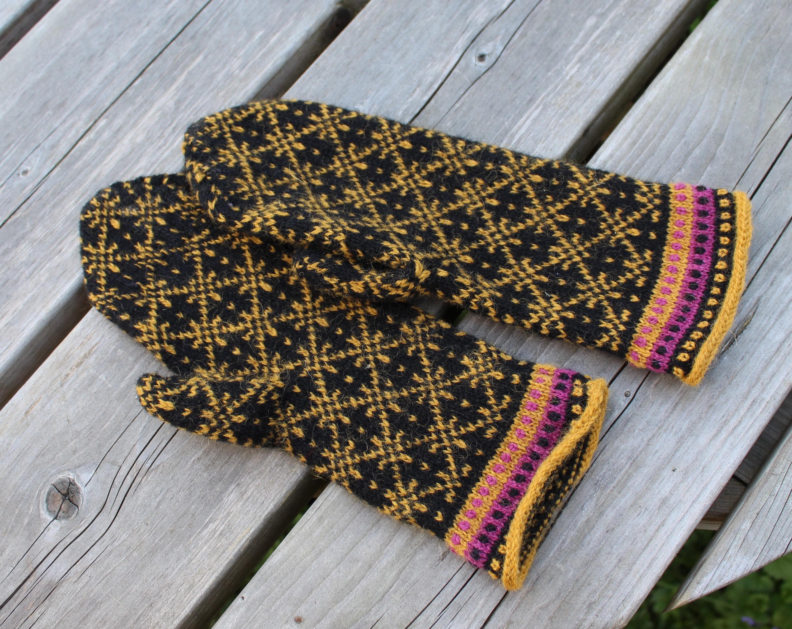 Pair of black and yellow patterned mittens on a wooden surface