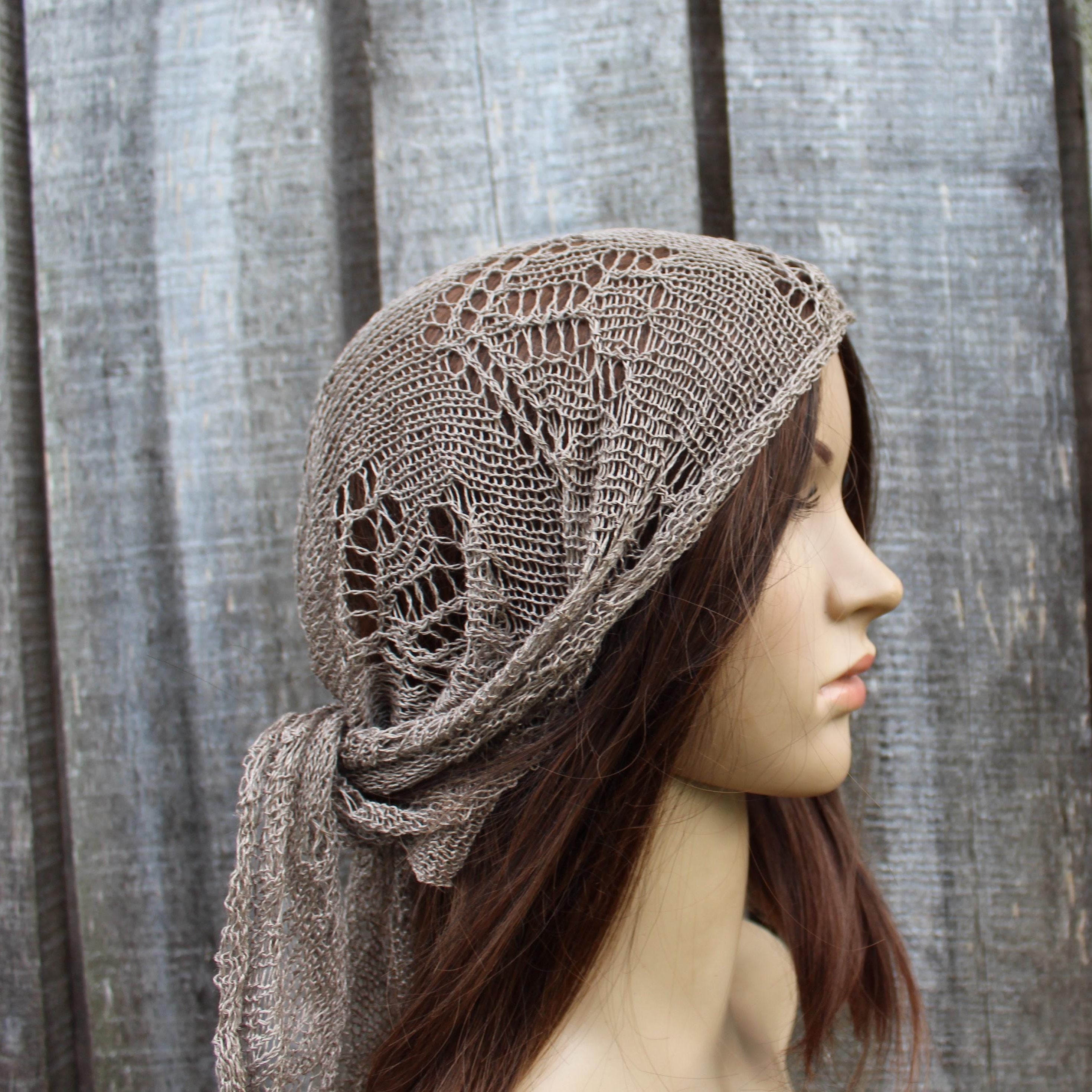 Mannequin head wearing a brown knitted headscarf -  bandana against a wooden fence background