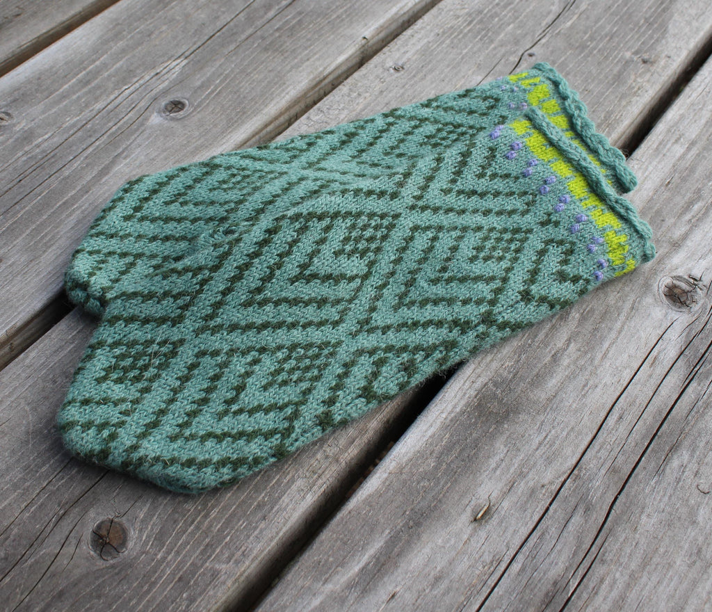 Green knitted mitten with a geometric pattern on a wooden surface