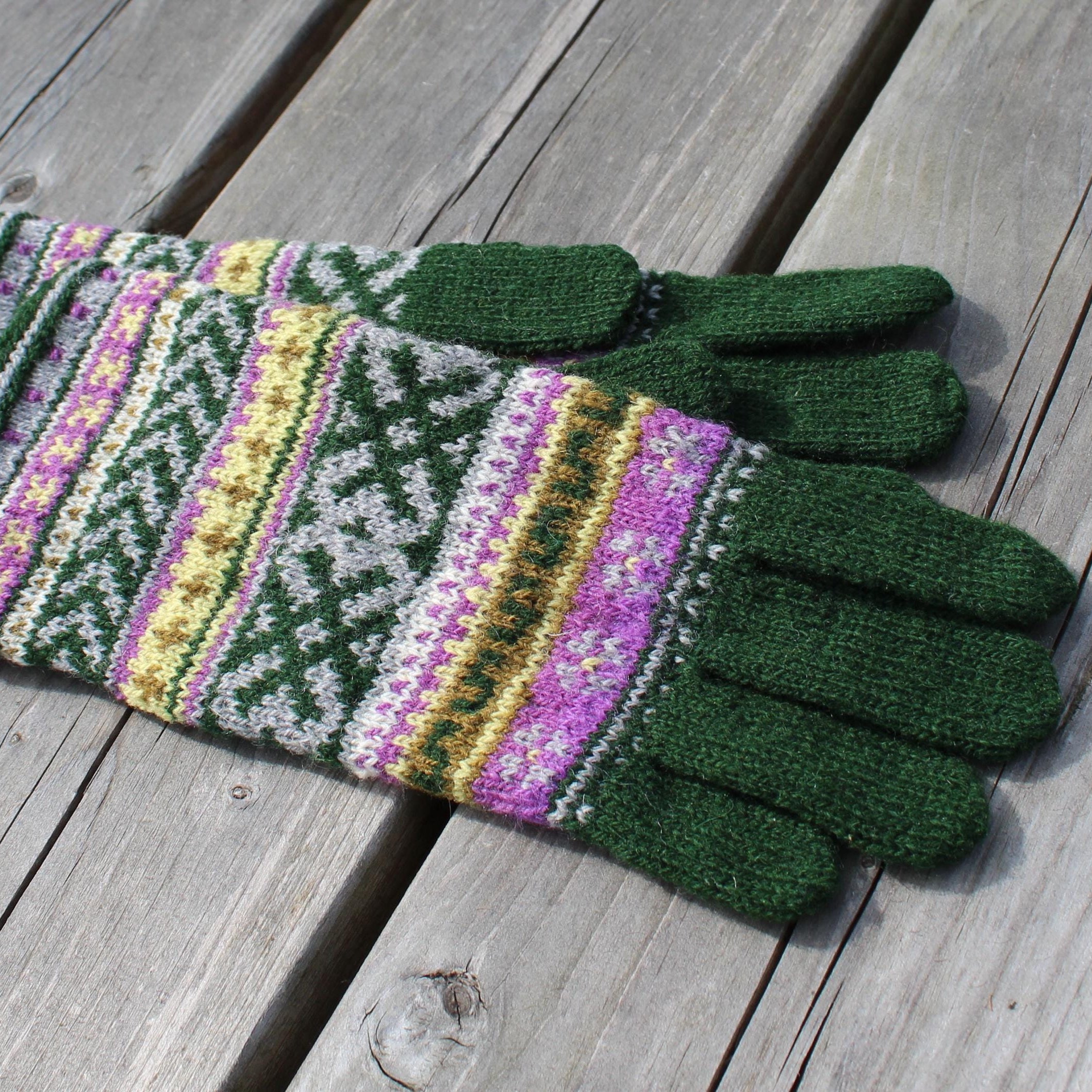 Pair of green gloves with colorful pattern on a wooden surface