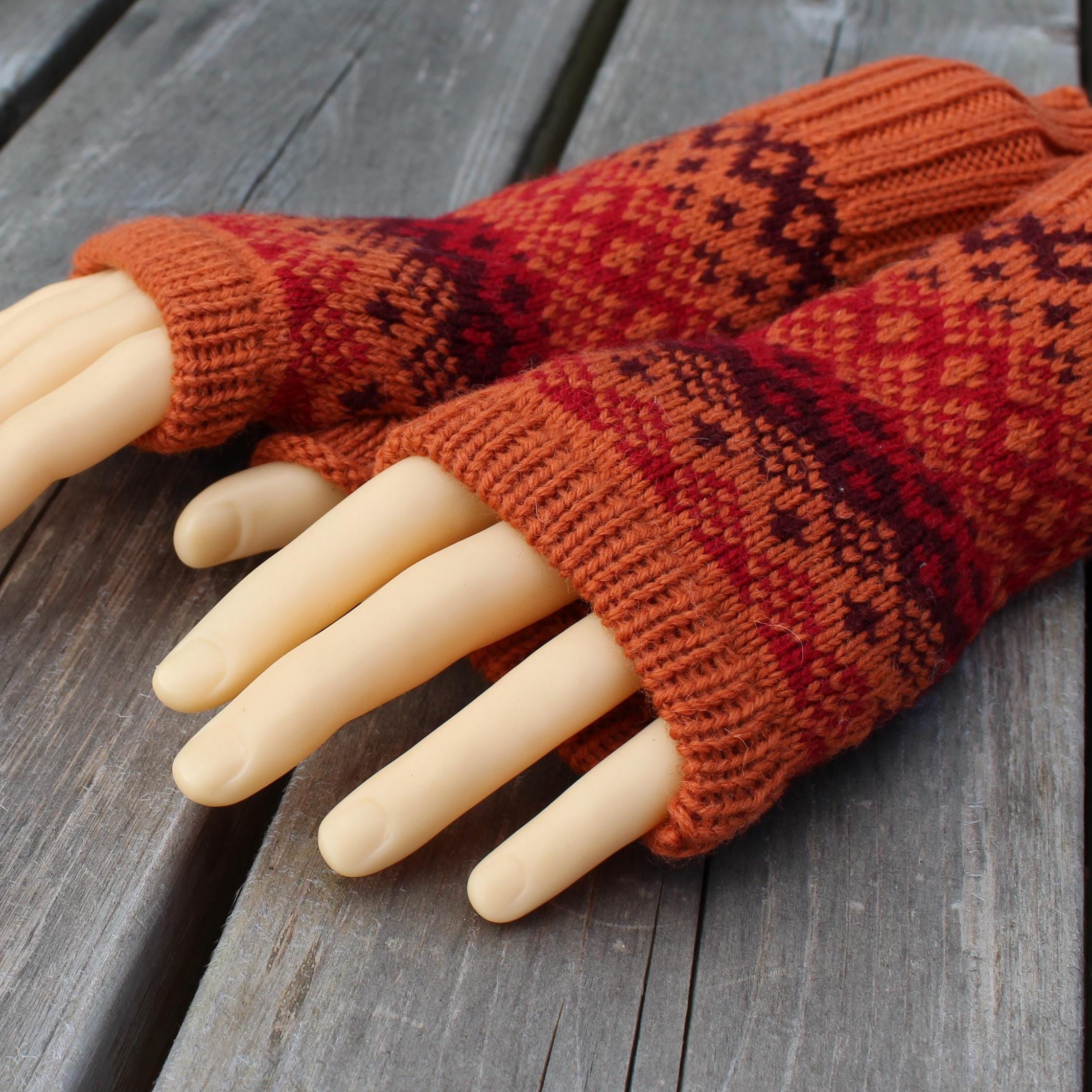 Pair of red and brown patterned fingerless gloves on a wooden surface