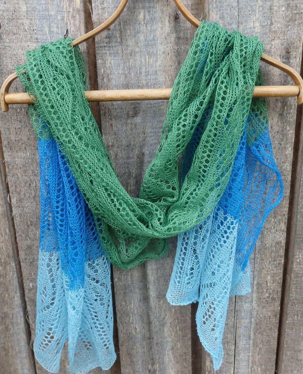 Green and blue lace scarf on a wooden hanger against a wooden background