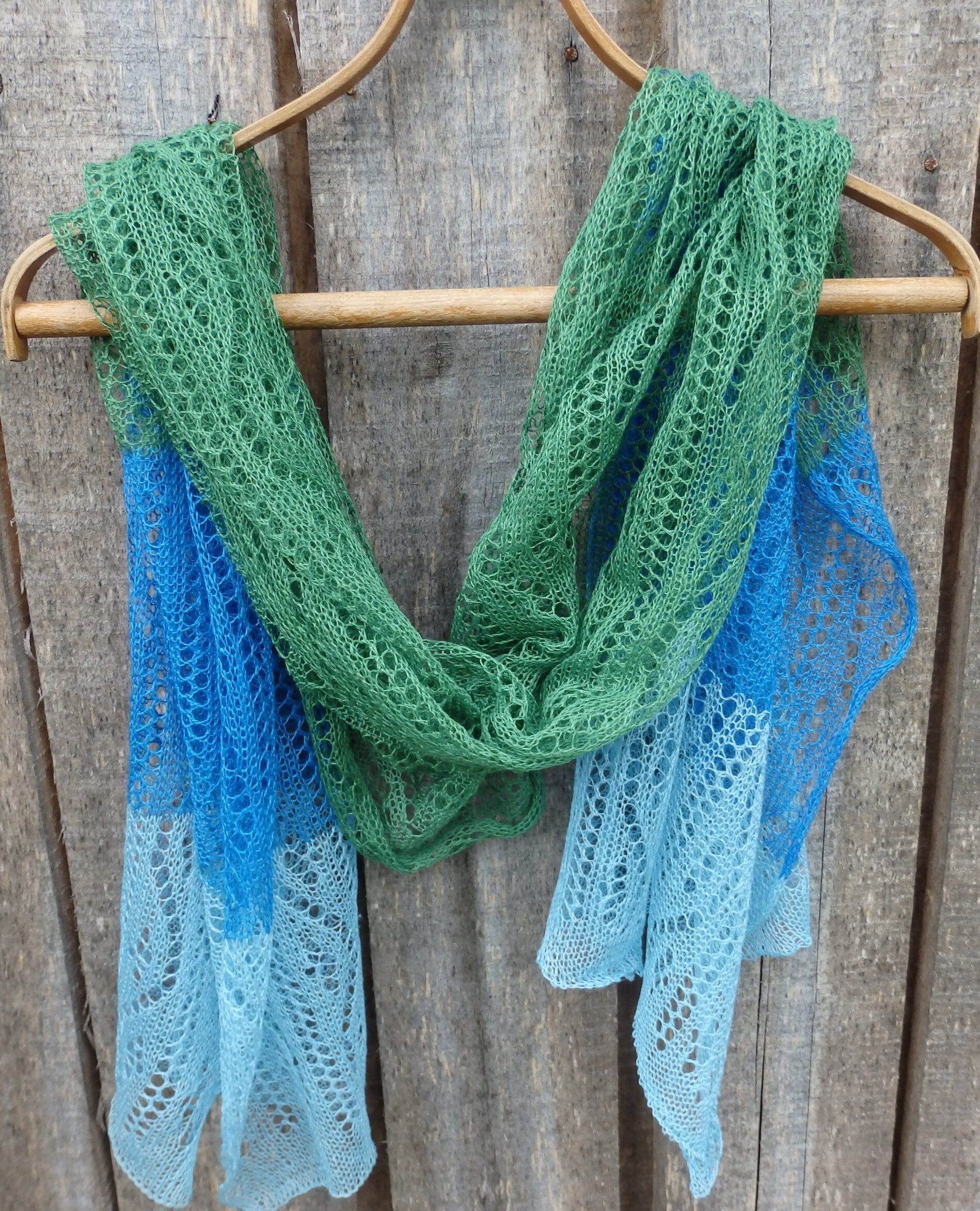Green and blue lace scarf on a wooden hanger against a wooden background