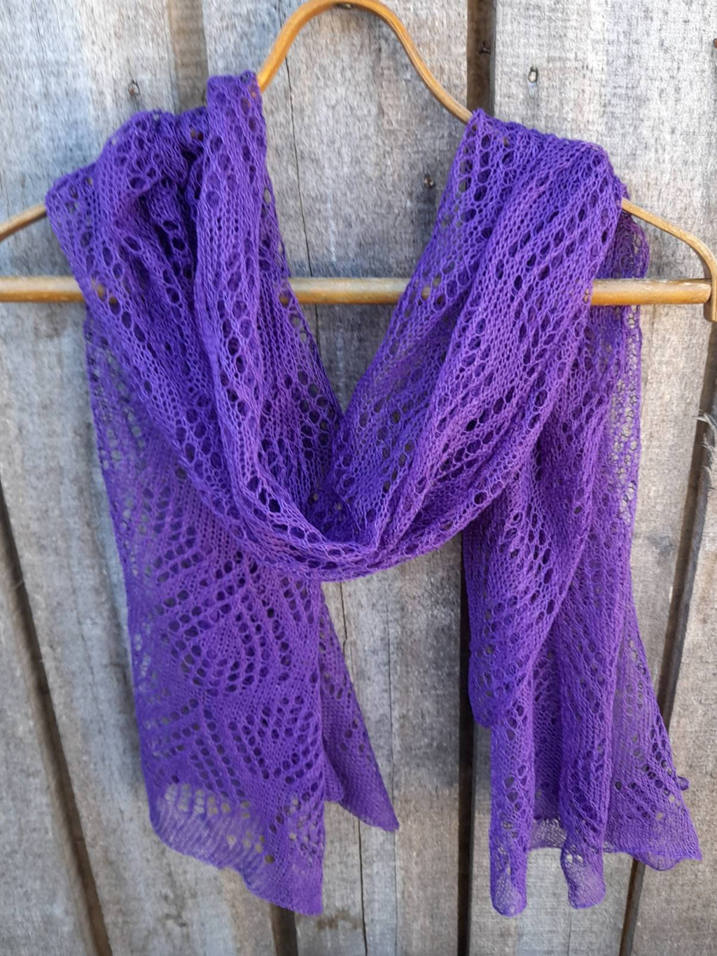Purple knitted shawl on a wooden hanger against a wooden background