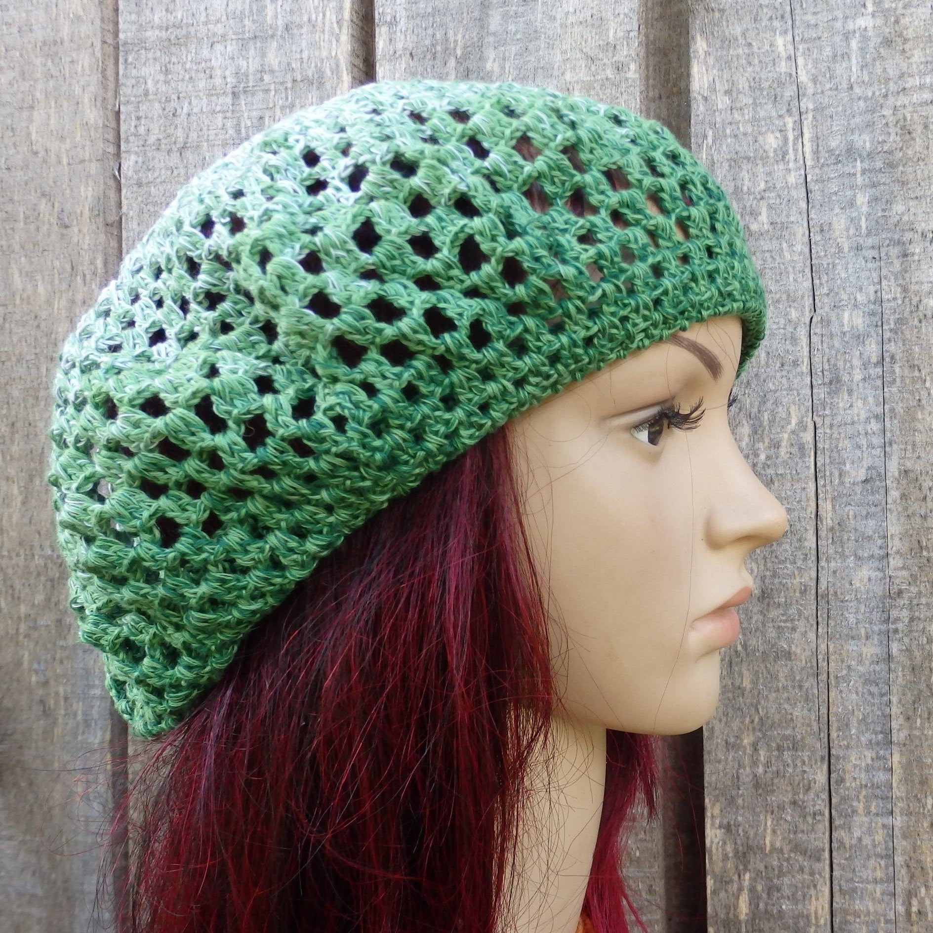 Green crochet hat on a mannequin head against a wooden background