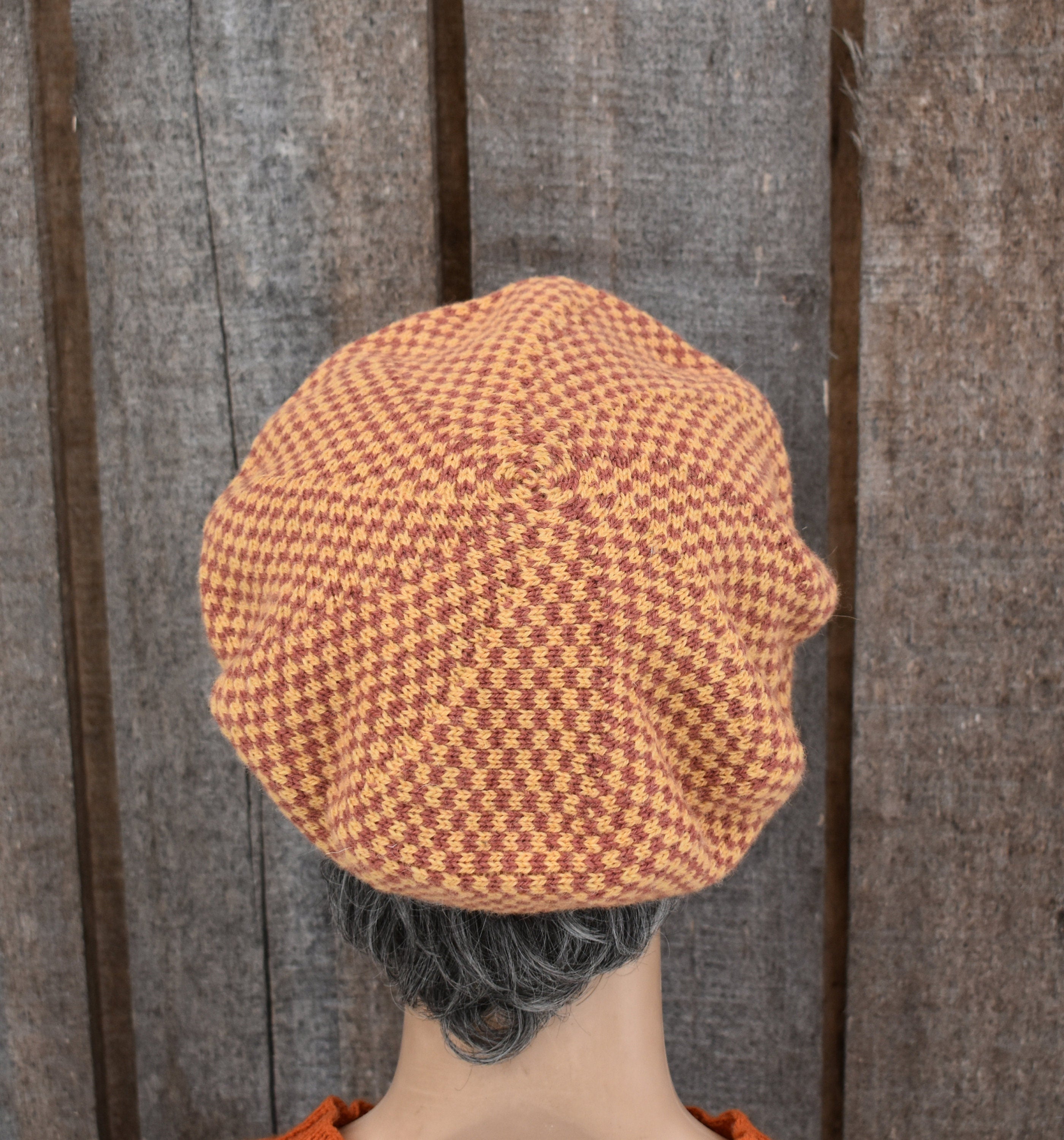 Person wearing a brown and orange checkered beanie against a wooden background