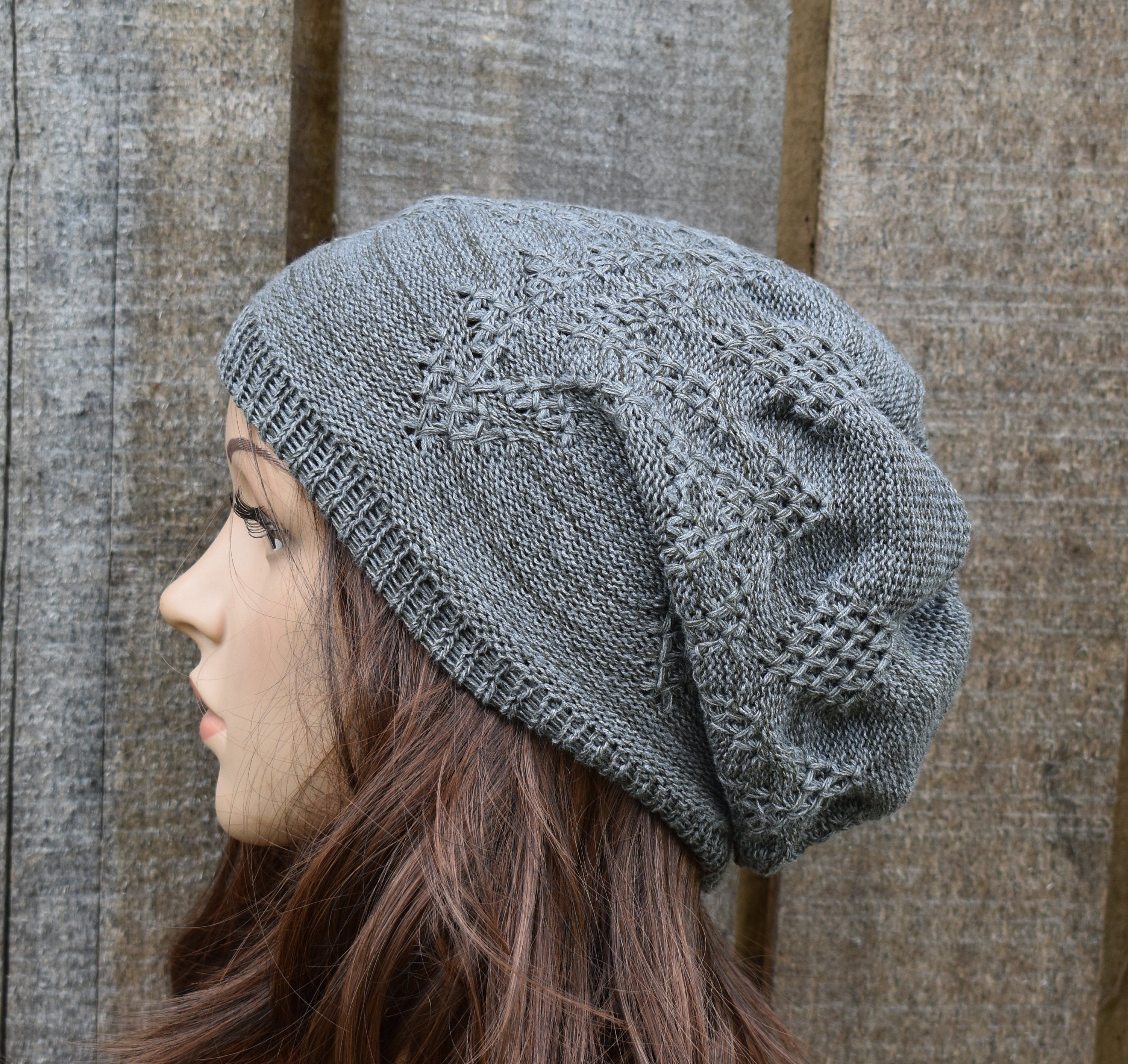 Person wearing a gray knit beanie with intricate patterns against a wooden background