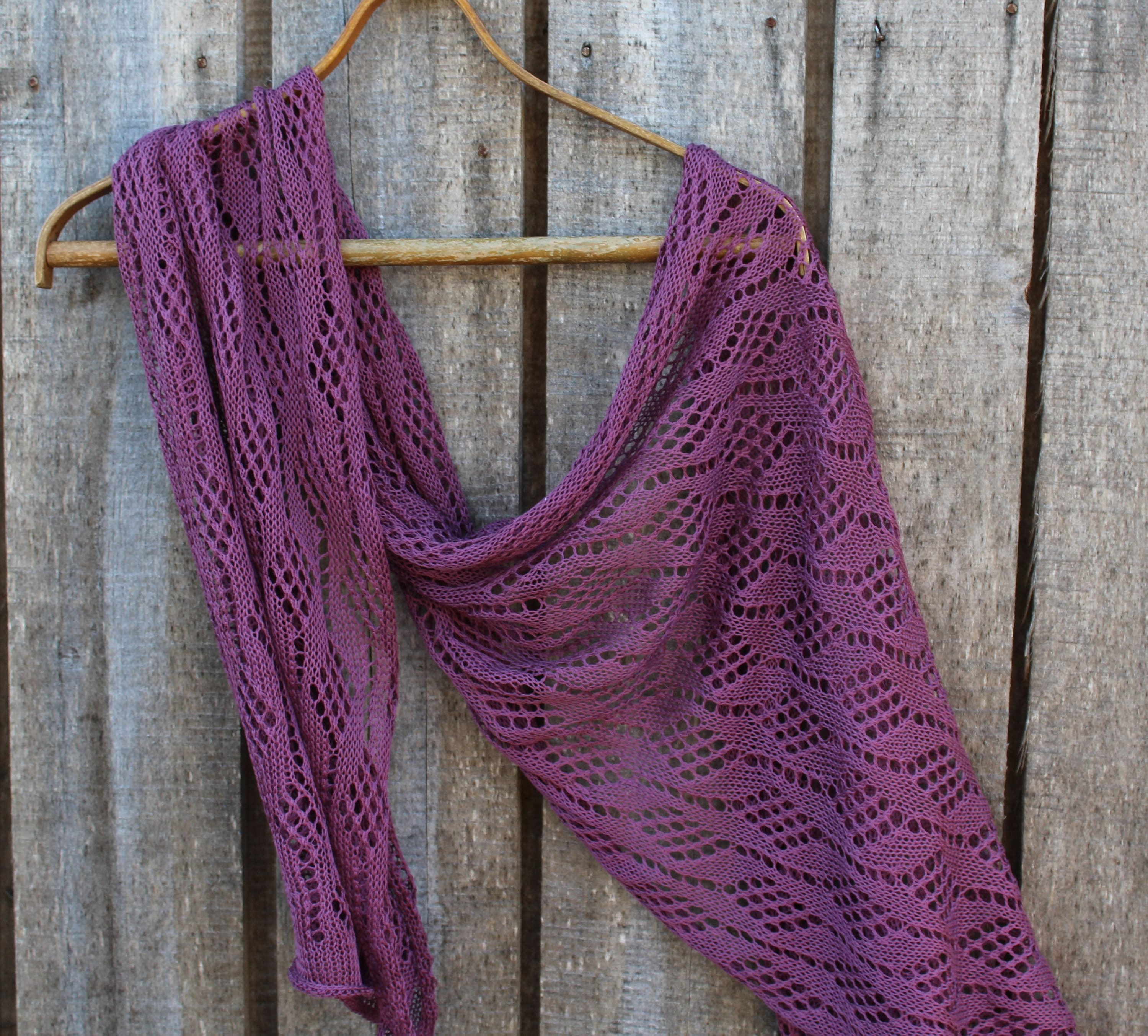 Purple knitted shawl draped over a wooden hanger against a rustic wooden background