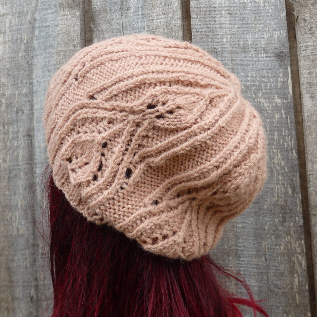Knitted beige beanie with intricate pattern on a wooden surface