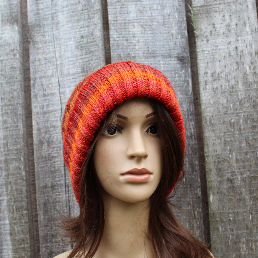 Mannequin head wearing a red and orange striped knit hat against a wooden panel background