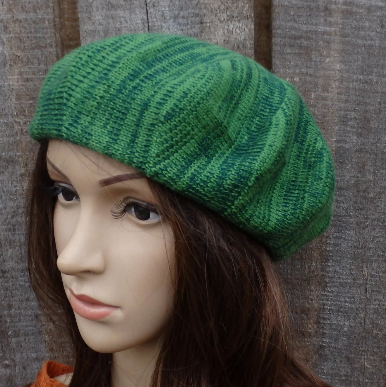 Green knitted beret on a mannequin head against a wooden background