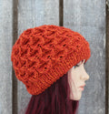 Orange knitted hat on a mannequin head against a wooden background