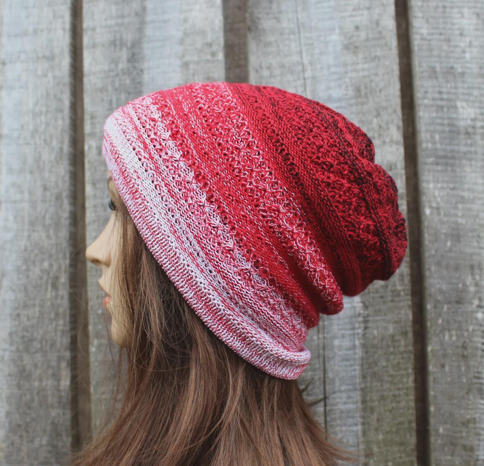 Person wearing a red and pink striped knit beanie against a wooden background
