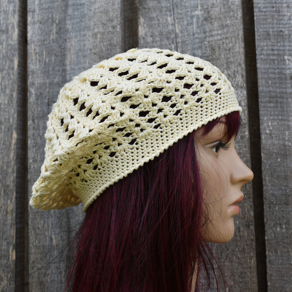Mannequin head wearing a cream-colored crochet hat against a wooden background