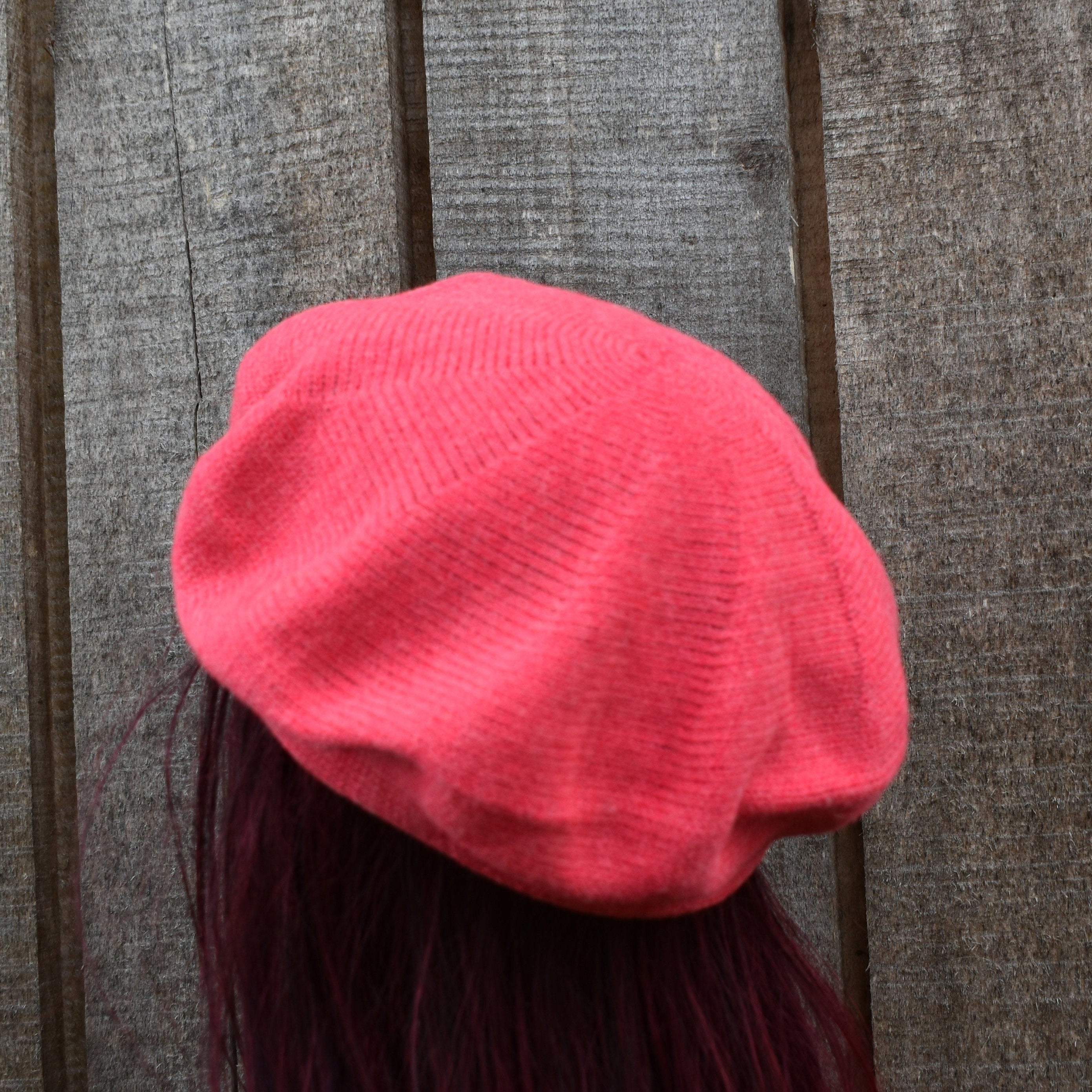 Pink knit beret worn by a person against a wooden background