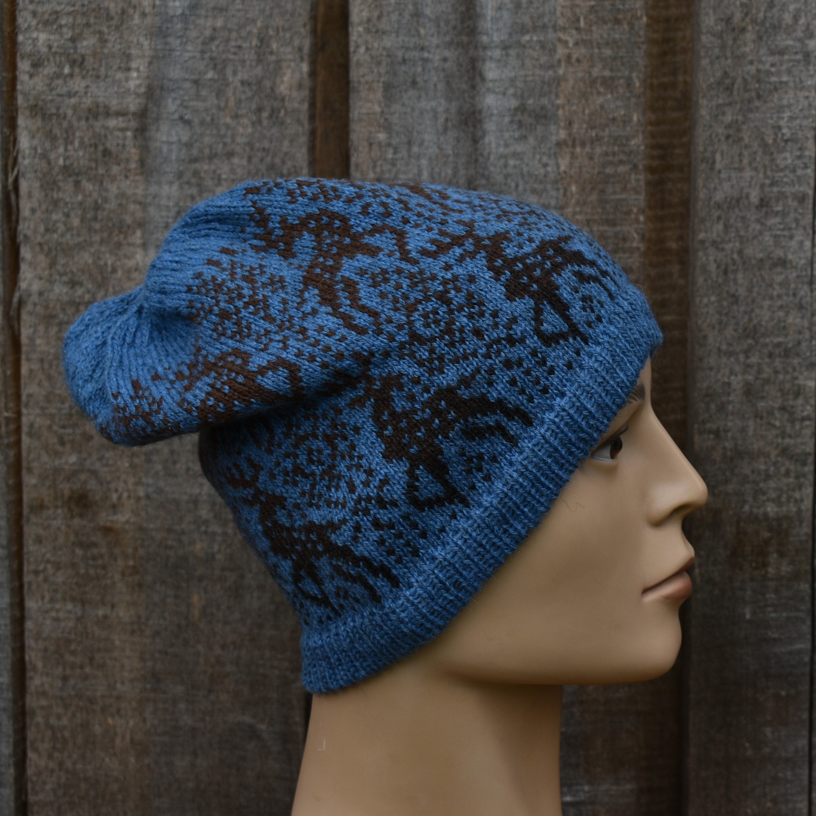 Blue knitted hat with black pattern on a mannequin head against a wooden background