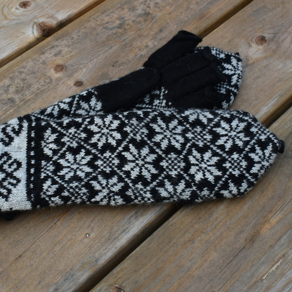 Pair of black and white patterned mittens on a wooden surface