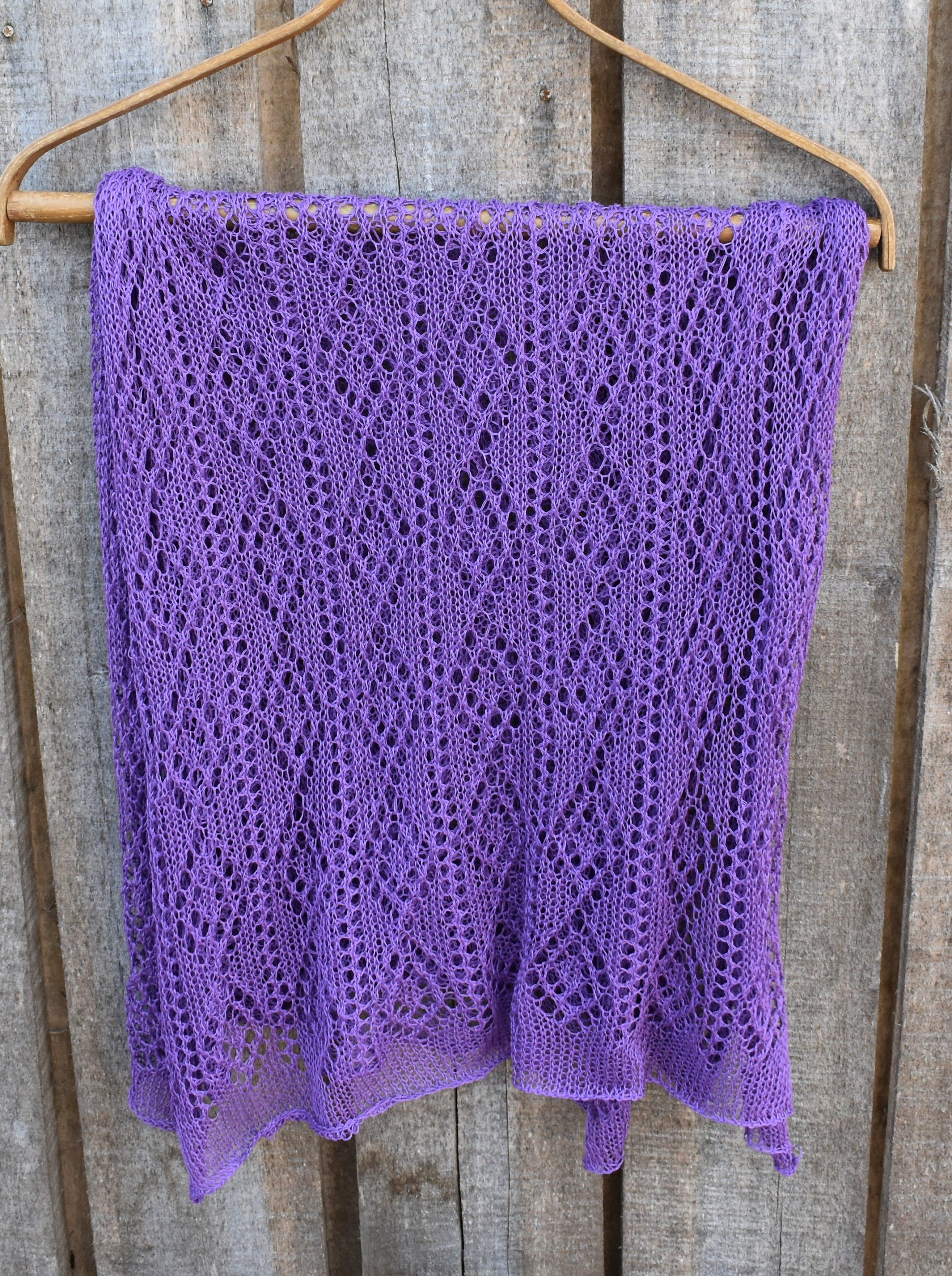 Purple knitted shawl on a wooden hanger against a wooden background
