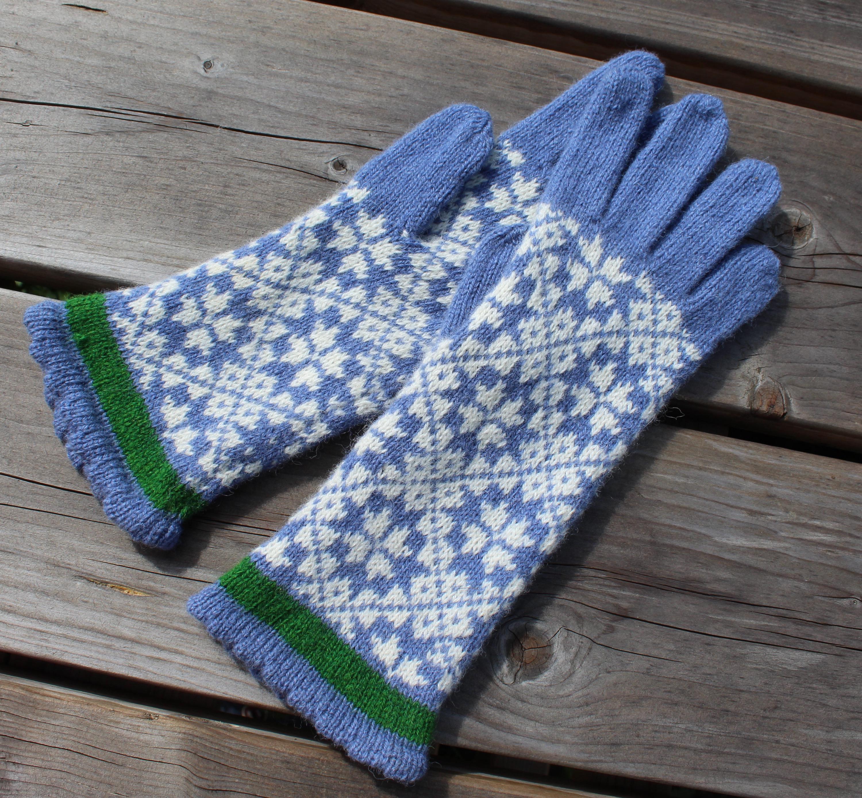 Pair of blue and white patterned gloves with green cuffs on a wooden surface