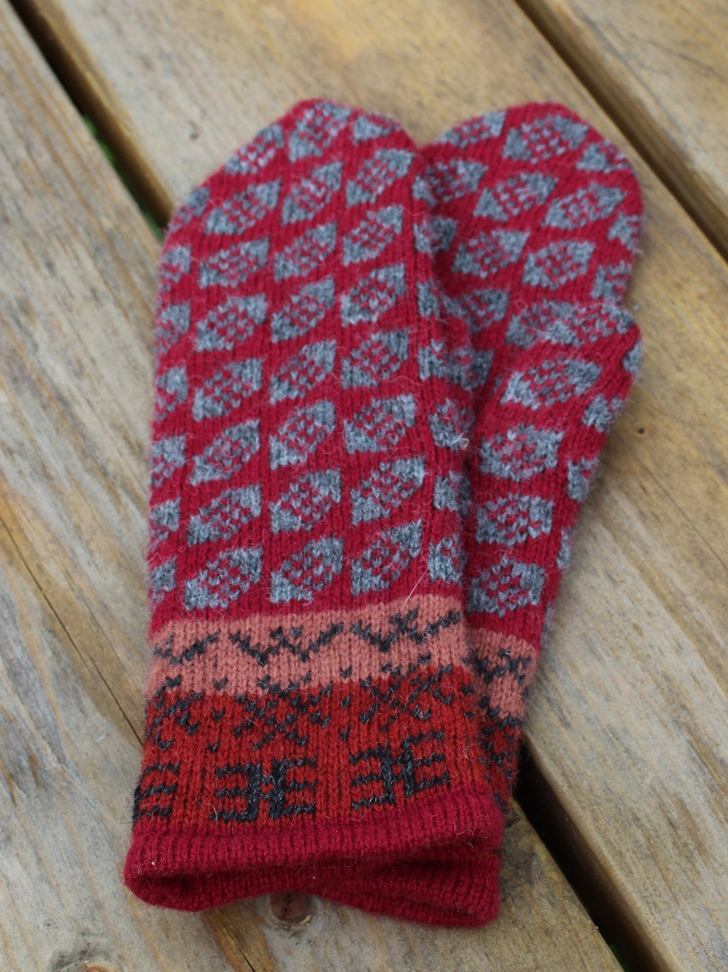 Red and gray patterned knitted mittens on a wooden surface