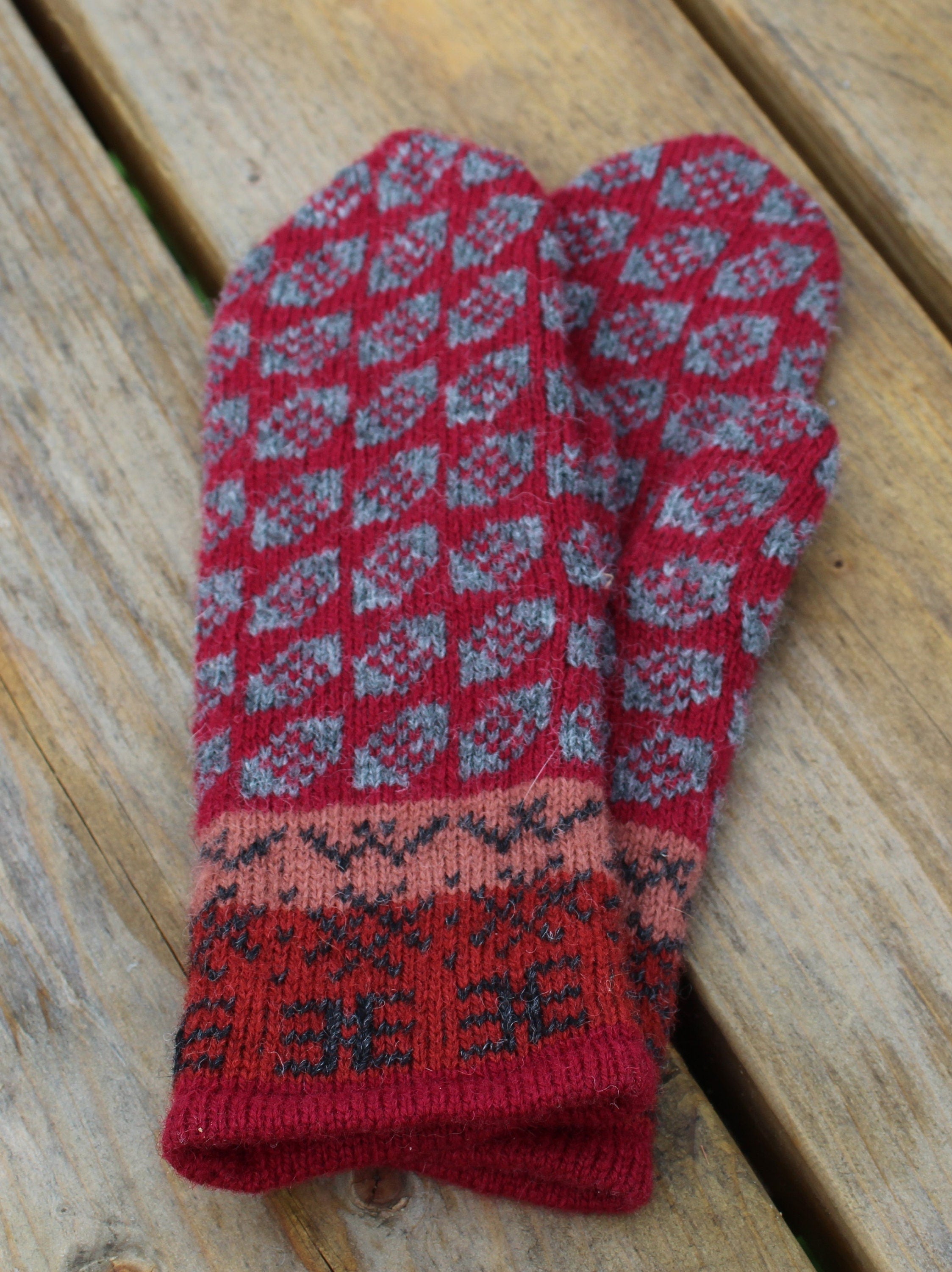 Red and gray patterned knitted mittens on a wooden surface
