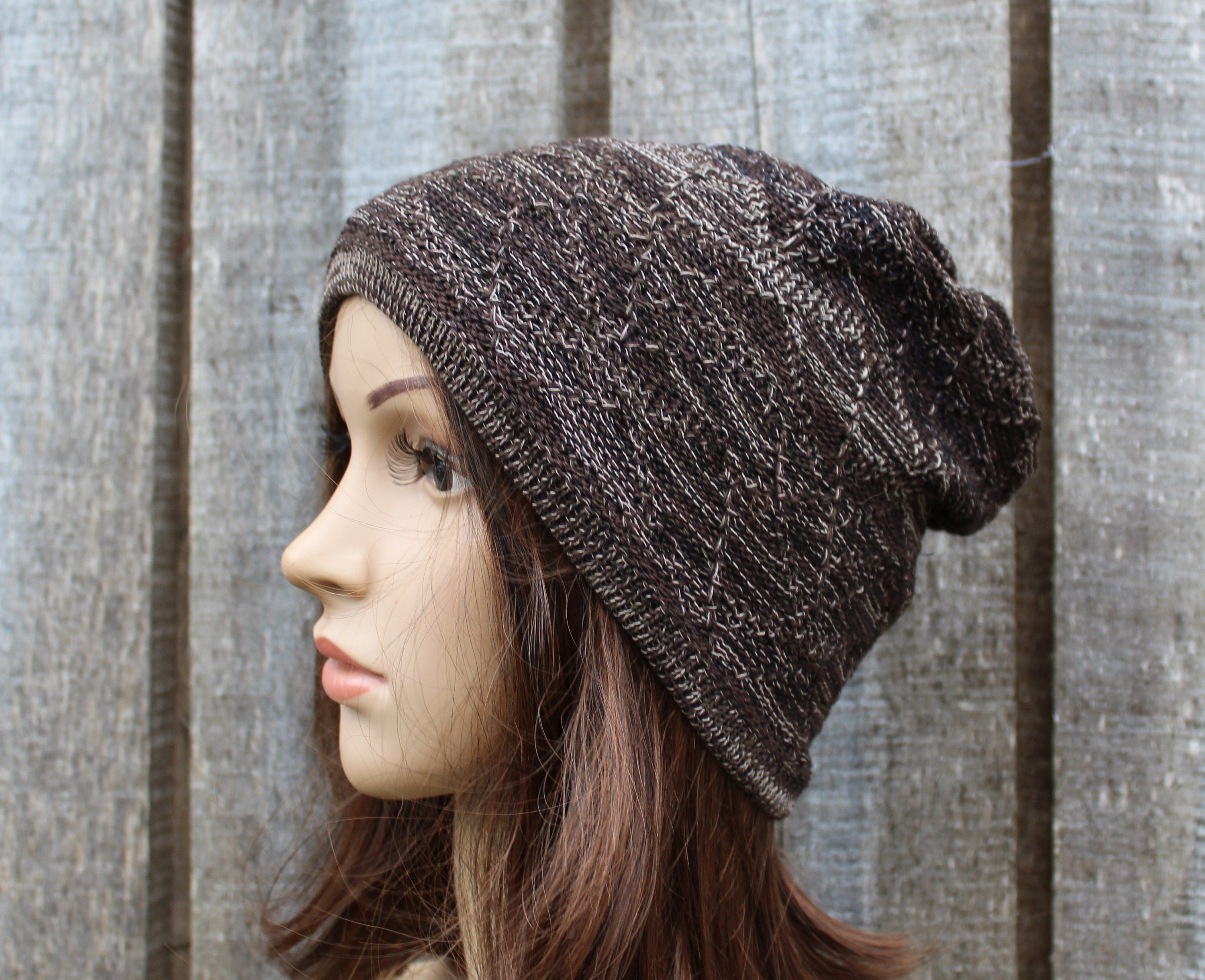 Knitted brown beanie on a mannequin head against a textured wall.
