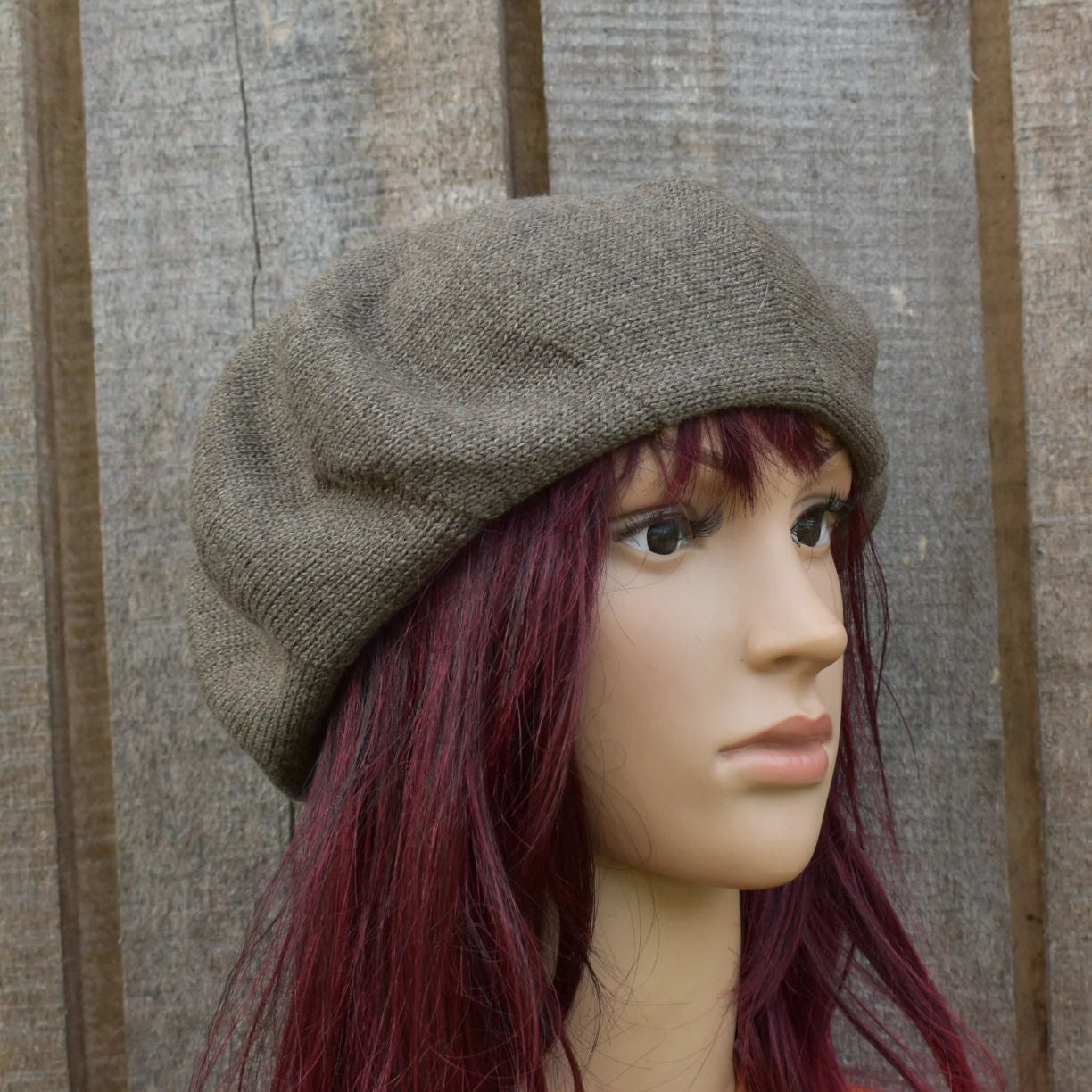 Mannequin head wearing a brown beret against a wooden panel background