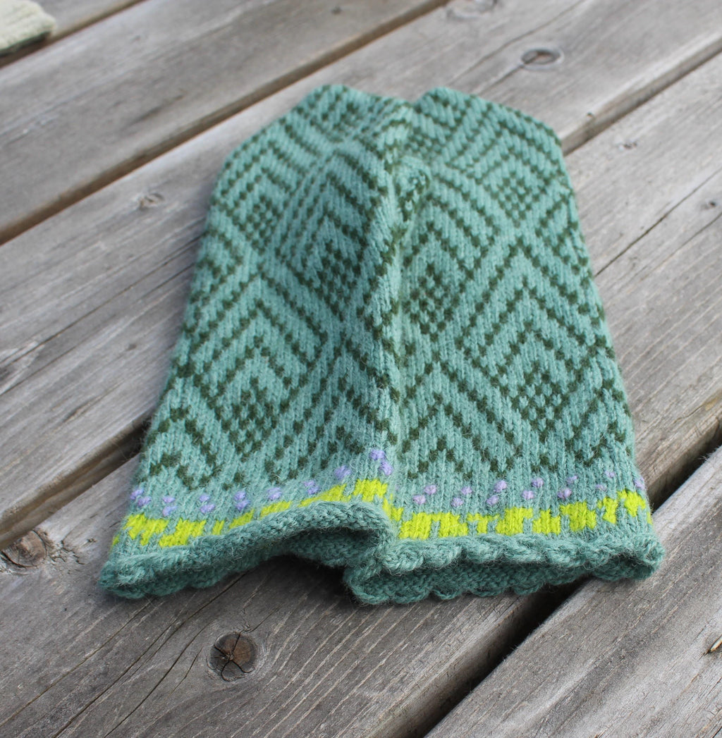 Knitted green baby romper with a pattern on a wooden surface