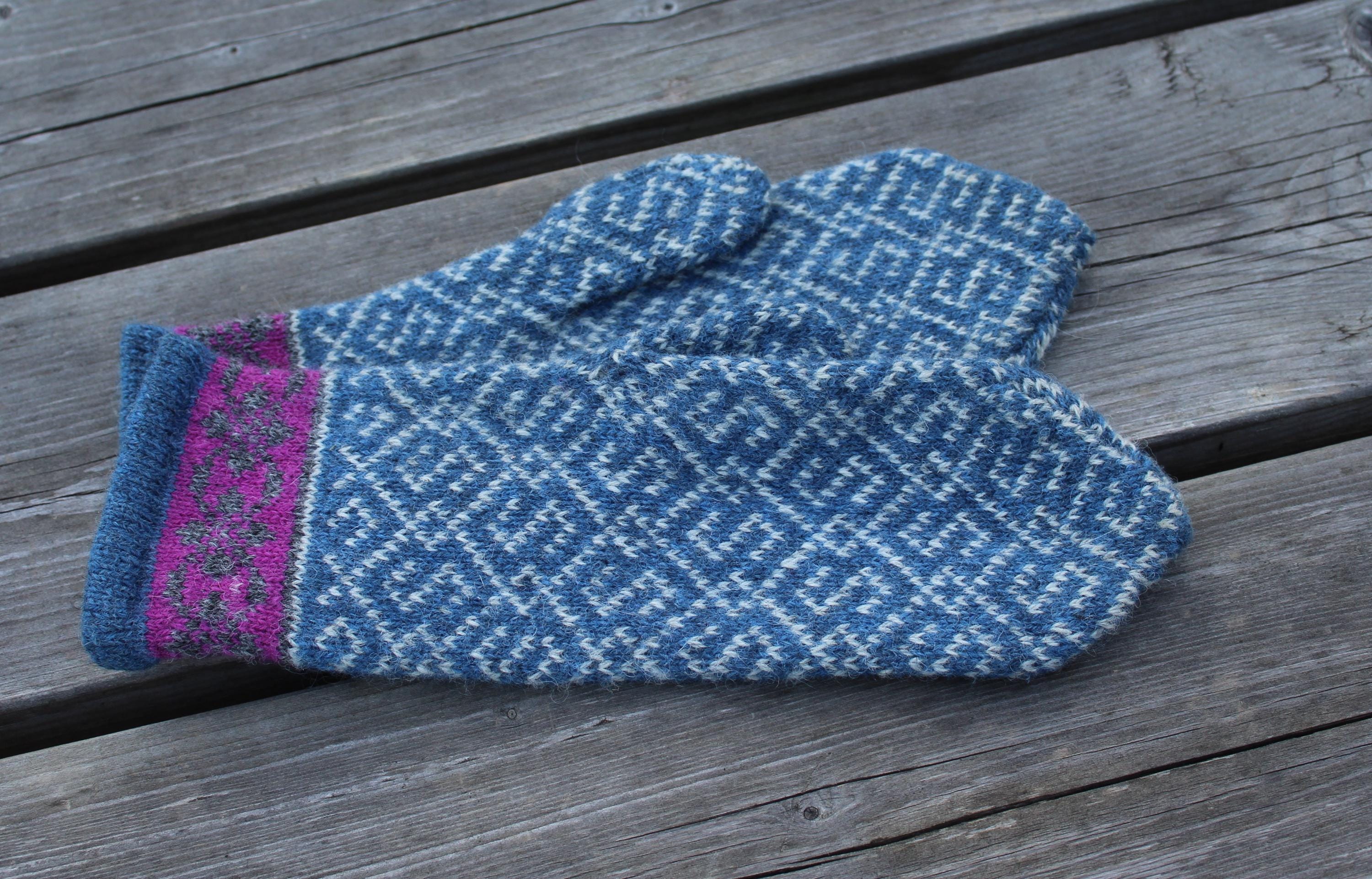 Pair of blue knitted mittens with a purple band on a wooden surface