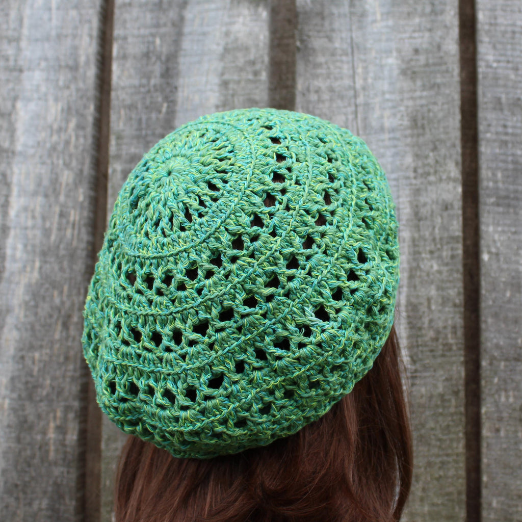 Green crocheted beanie worn by a person with brown hair against a wooden background