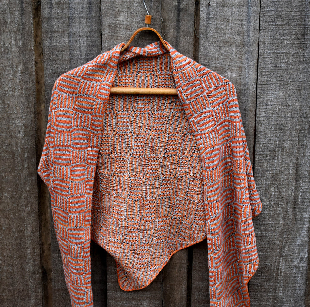 Knitted shawl with orange and brown pattern on a wooden hanger against a wooden background